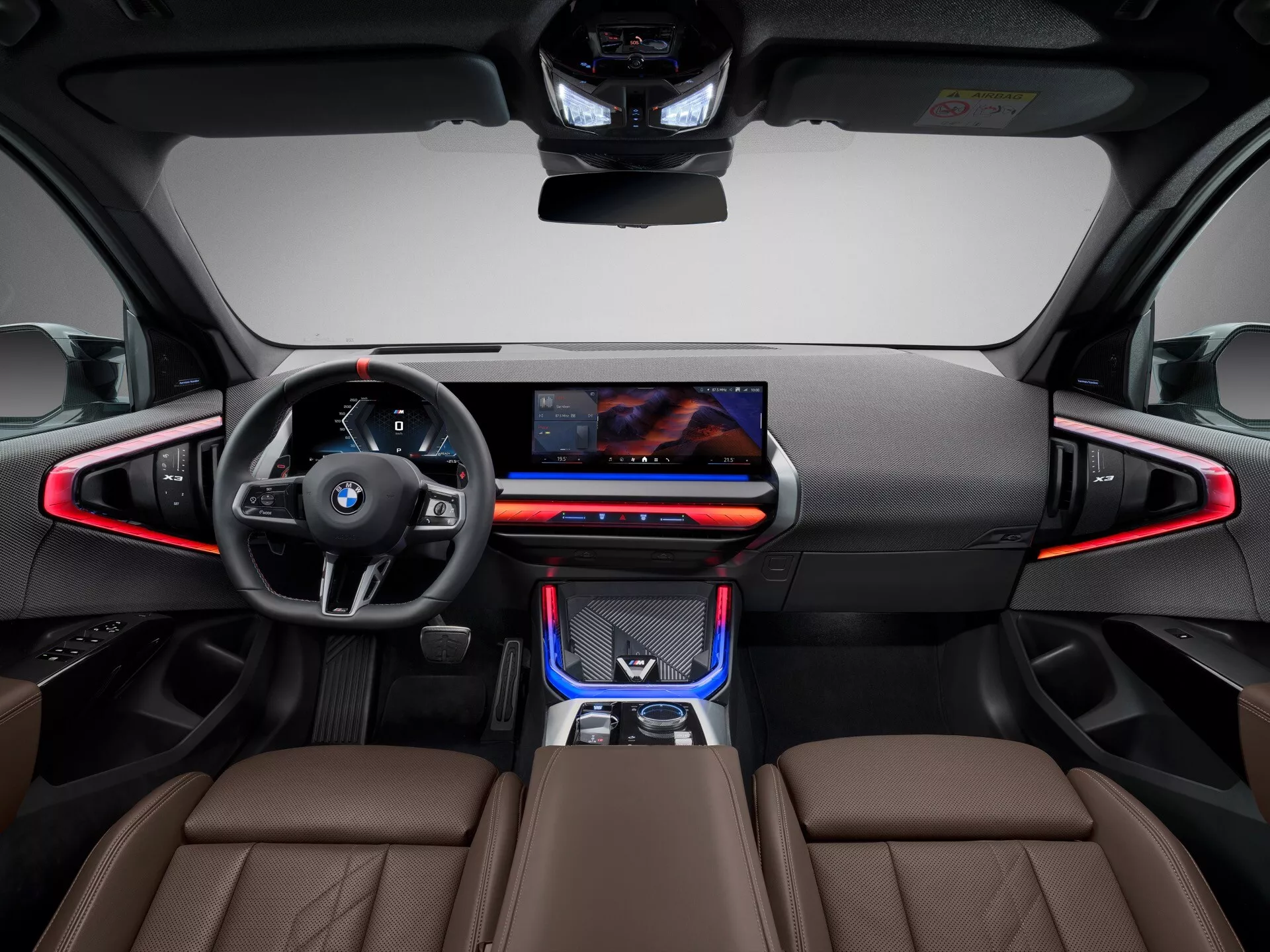 Widok wnętrza BMW X3 2024 (G45) z perspektywy tylnego siedzenia, prezentujący skórzaną, wielofunkcyjną kierownicę z emblematem BMW, szeroki centralny ekran dotykowy, czerwonawe oświetlenie ambientowe, smukłe kratki wentylacyjne i dotykowe elementy sterujące, elegancki selektor biegów na konsoli środkowej, sportowe przednie siedzenia w skórzanej tapicerce ze znacznym wsparciem bocznym oraz dwukolorowy schemat kolorystyczny czerni i brązu zaakcentowany wysokiej jakości materiałami dla nowoczesnego i luksusowego efektu.