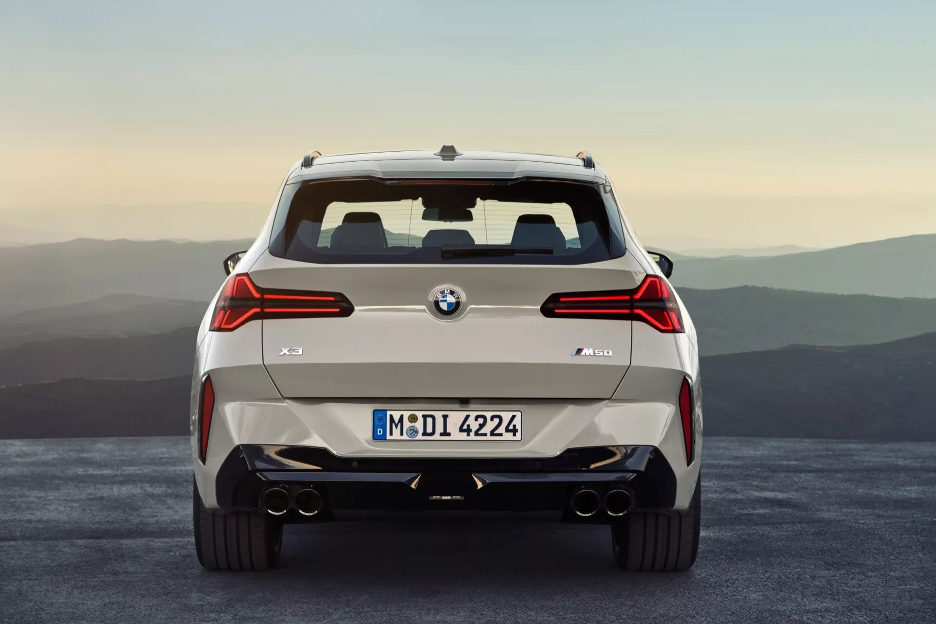 Tylny widok BMW X3 2024 (G45), z widocznym znakiem BMW i oznaczeniem modelu 'X3 M40i'. Zdjęcie prezentuje symetryczną kompozycję z prostej, poziomej perspektywy, ukazując pełną szerokość pojazdu. Charakterystyczne trójwymiarowe tylne światła LED, wyraźne wloty powietrza w tylnym zderzaku, srebrne wykończenia oraz podwójne wydechy po obu stronach podkreślają design ukierunkowany na osiągi samochodu. Centralnie zamontowana tablica rejestracyjna i tylna osłona wskazują na solidny wygląd i zdolność do lekkiego off-roadu.