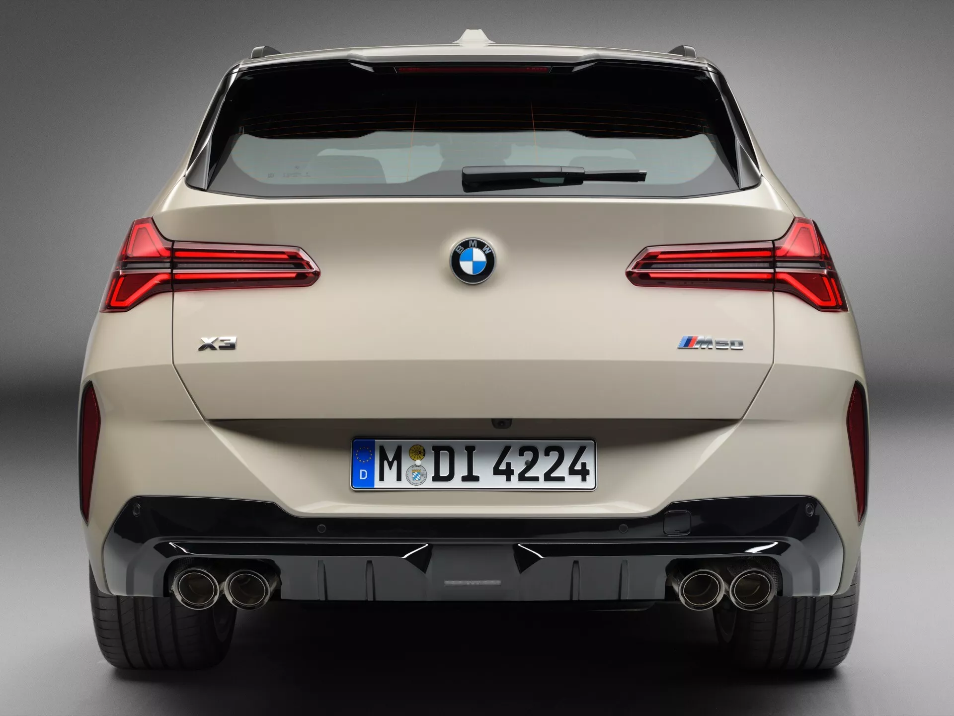 Widok tylnej części BMW X3 (G45) M40i z 2024 roku, nowoczesnego i luksusowego SUV-a, ukazujący charakterystyczne cechy, takie jak ostro stylizowane tylne światła, podwójne końcówki wydechu, tylne czujniki parkowania, tylny dyfuzor, odblaskowy pasek na dolnej części tylnego zderzaka i tylna wycieraczka, sfotografowane z nieco podwyższonej perspektywy.