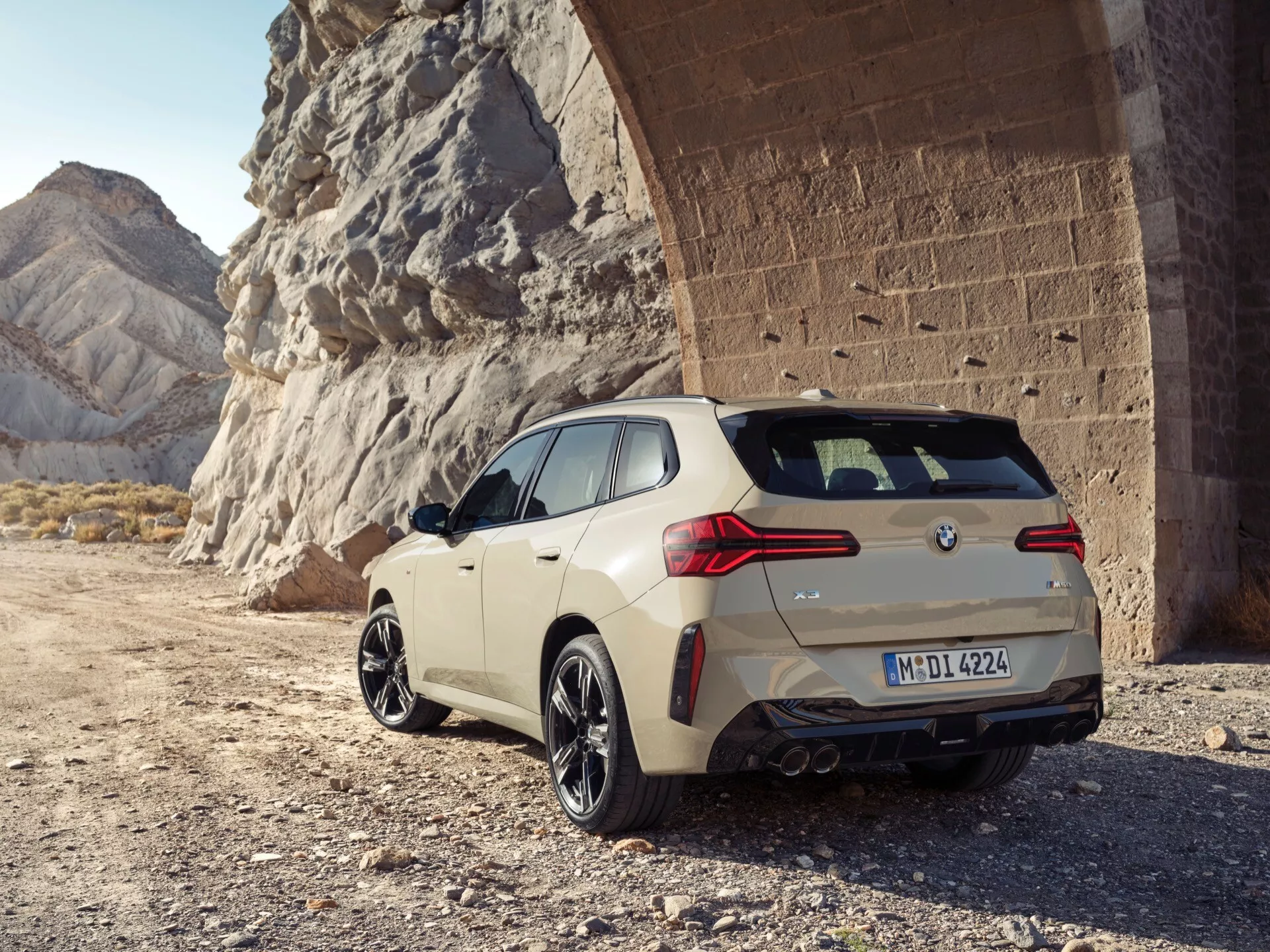 Widok samochodu typu hatchback z tyłu pod kątem na kamienistym podłożu. Pojazd cechuje się eleganckimi, aerodynamicznymi liniami, tylnym spojlerem, podwójnymi rurami wydechowymi, dużymi felgami wieloramiennymi z oponami niskoprofilowymi oraz zaawansowaną aerodynamiką. Jego poziome tylne światła podkreślają szerokość samochodu. Zdjęcie przedstawia samochód na świeżym powietrzu w naturalnym oświetleniu, z kamiennym krajobrazem stanowiącym solidne, przygodowe tło.