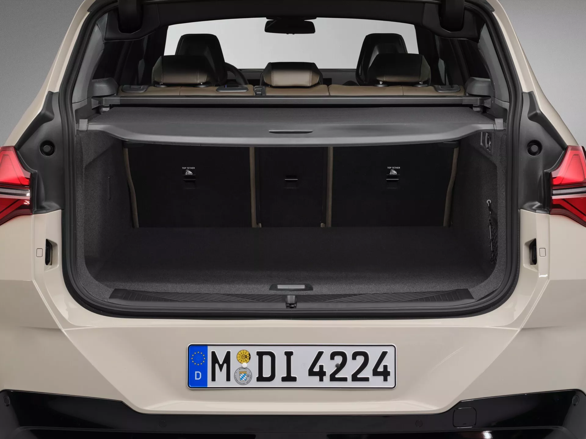 Widok tylni BMW X3 2024 (G45) z otwartym bagażnikiem, ukazujący pełną, nieprzesłoniętą przestrzeń ładunkową. Symetryczne ujęcie zewnętrzne podkreśla podwyższoną podłogę przestrzeni ładunkowej, nowoczesne tylne światła z technologią LED i nieskazitelny stan wykładziny wewnętrznej. Tablica rejestracyjna wskazuje na rejestrację w Niemczech. Prezentuje pojemność ładunkową ze złożonymi tylnymi siedzeniami i chowaną osłoną ładunkową.