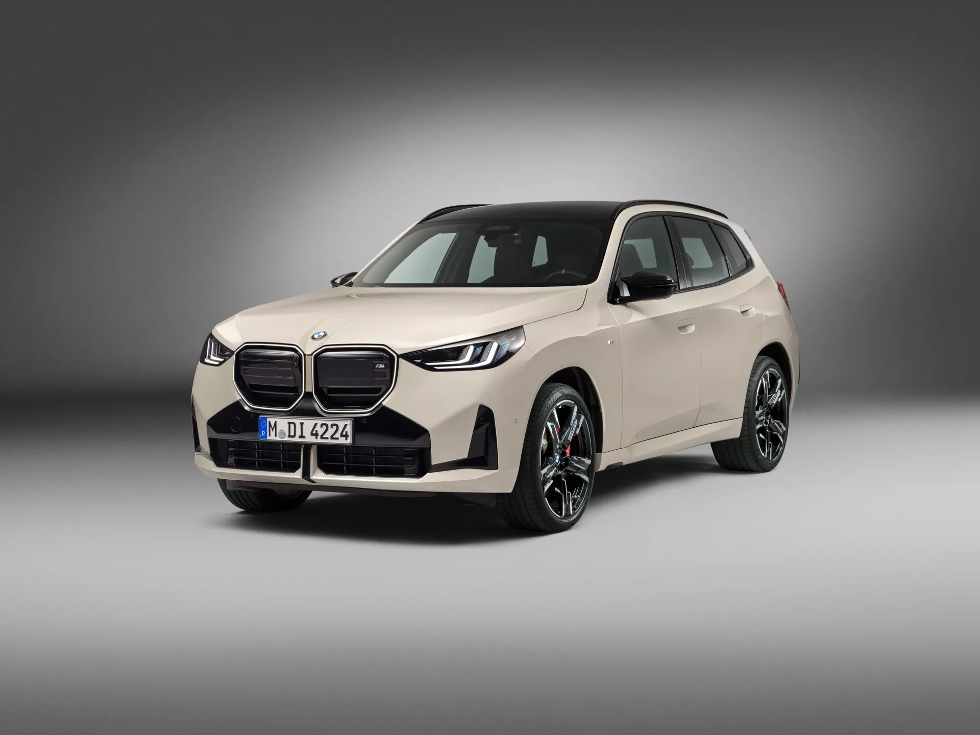 Studyjna fotografia współczesnego luksusowego kompaktowego SUV/Crossover, BMW X3 2024 (G45), ukazana w widoku z trzech czwartych od przodu, podkreślająca przednią część z charakterystycznym grillem w kształcie nerki, eleganckimi reflektorami z światłami do jazdy dziennej i światłami przeciwmgielnymi na zderzaku. Duże, aluminiowe koła samochodu mają nowoczesny, wieloszprychowy design. Kolor nadwozia to jasny, neutralny odcień z gładkimi liniami i aerodynamicznymi konturami. Lusterka boczne mają zintegrowane kierunkowskazy, a tylne szyby są przyciemniane. Pojazd jest wyśrodkowany, z dużą ilością jest przestrzeni wokół, sfotografowany w miękkim, rozproszonym oświetleniu studyjnym z gradientowym tłem.