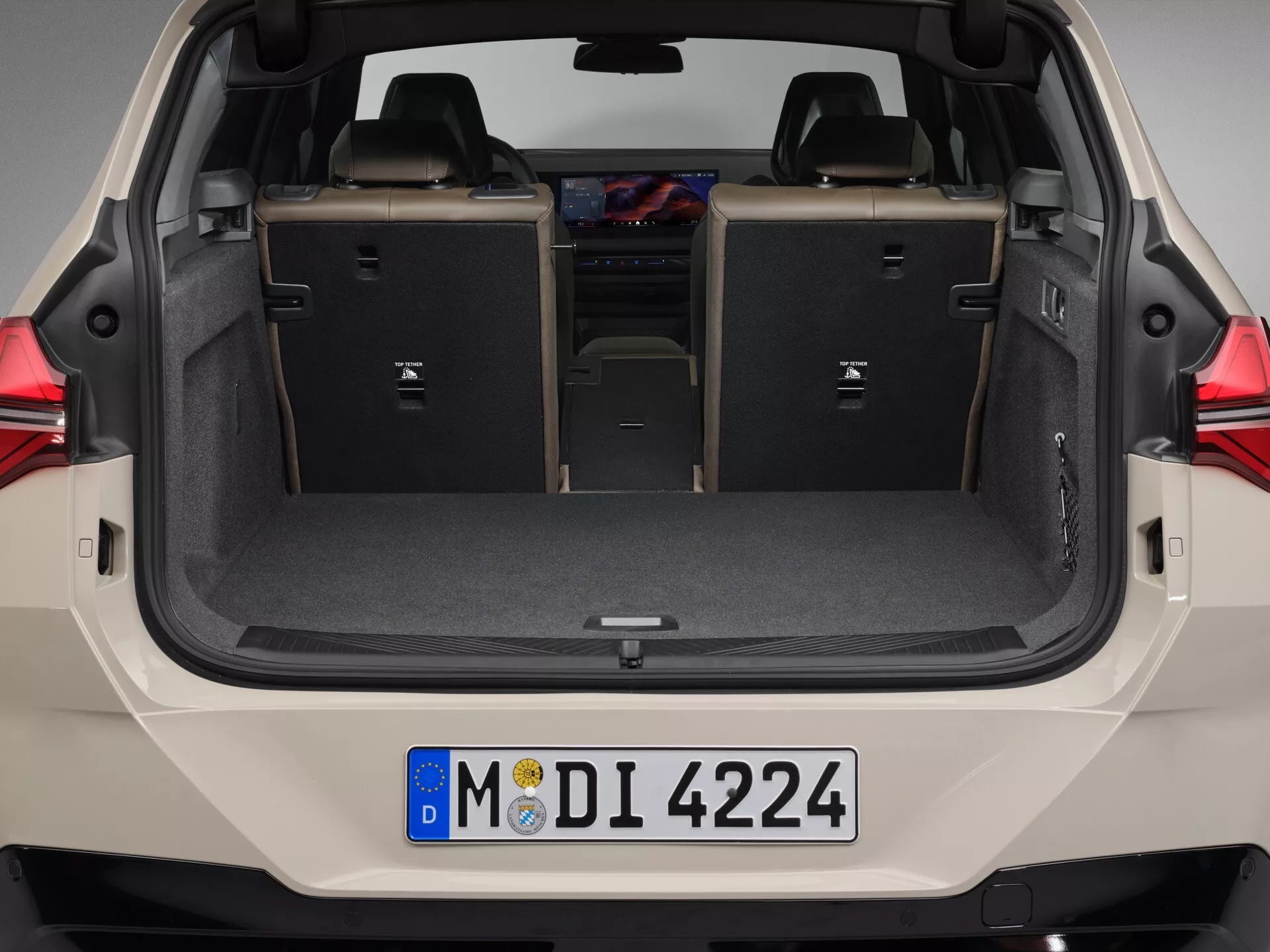 Widok tylny BMW X3 2024 (G45) z otwartym bagażnikiem pokazujący przestronną przestrzeń ładunkową, płaską podłogę bagażnika, złożone tylne siedzenia w konfiguracji 60/40 oraz wysuwaną osłonę dla zachowania prywatności. Widoczny jest wystrój wnętrza tylnej klapy, tylny zderzak i część tylnych świateł, co sugeruje nowoczesny design i elastyczną pojemność magazynowania.