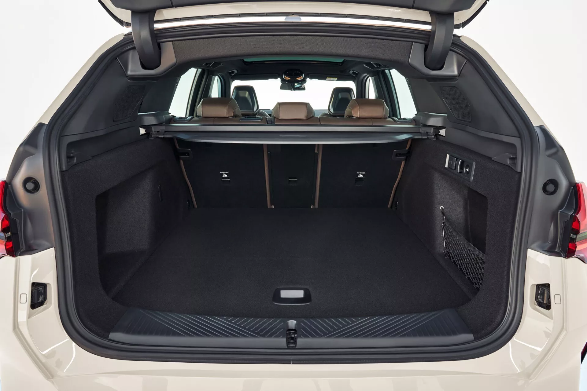 Czysty widok na bagażnik BMW X3 2024 (G45) z tylnej perspektywy z otwartą pokrywą bagażnika, ukazujący przestronną, czystą i ciemno wykładzinową przestrzeń. Bagażnik ma punkty mocowania, boczną przegrodę z siatką na bagaż oraz poziomą barierę za tylnymi siedzeniami.