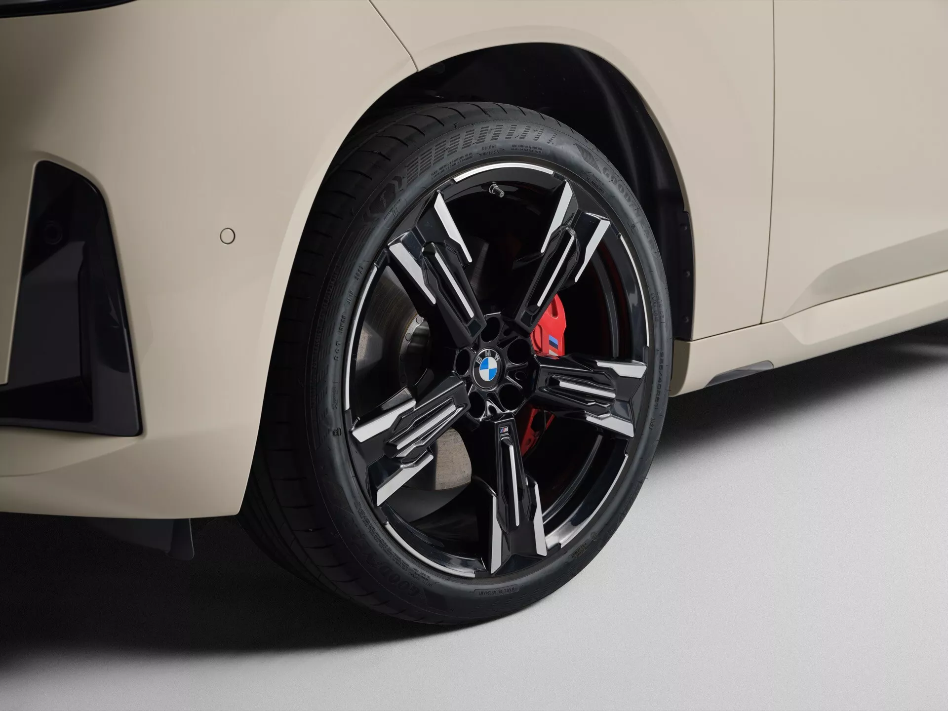 Zbliżenie na koło i boczną część nadwozia BMW X3 2024 (G45). Zawiera aluminiowe koło o nowoczesnym, wieloramiennym designie i czerwony, wysokowydajny zacisk hamulcowy. Opona niskoprofilowa wskazuje na nacisk na prowadzenie i estetykę. Jasny kolor nadwozia kontrastuje z ciemnym kołem. Widoczny boczny wlot powietrza oraz zintegrowana dolna spódnica sugerują projekt ukierunkowany na wydajność. Miękkie, rozproszone oświetlenie w ustawieniu studyjnym podkreśla szczegóły.