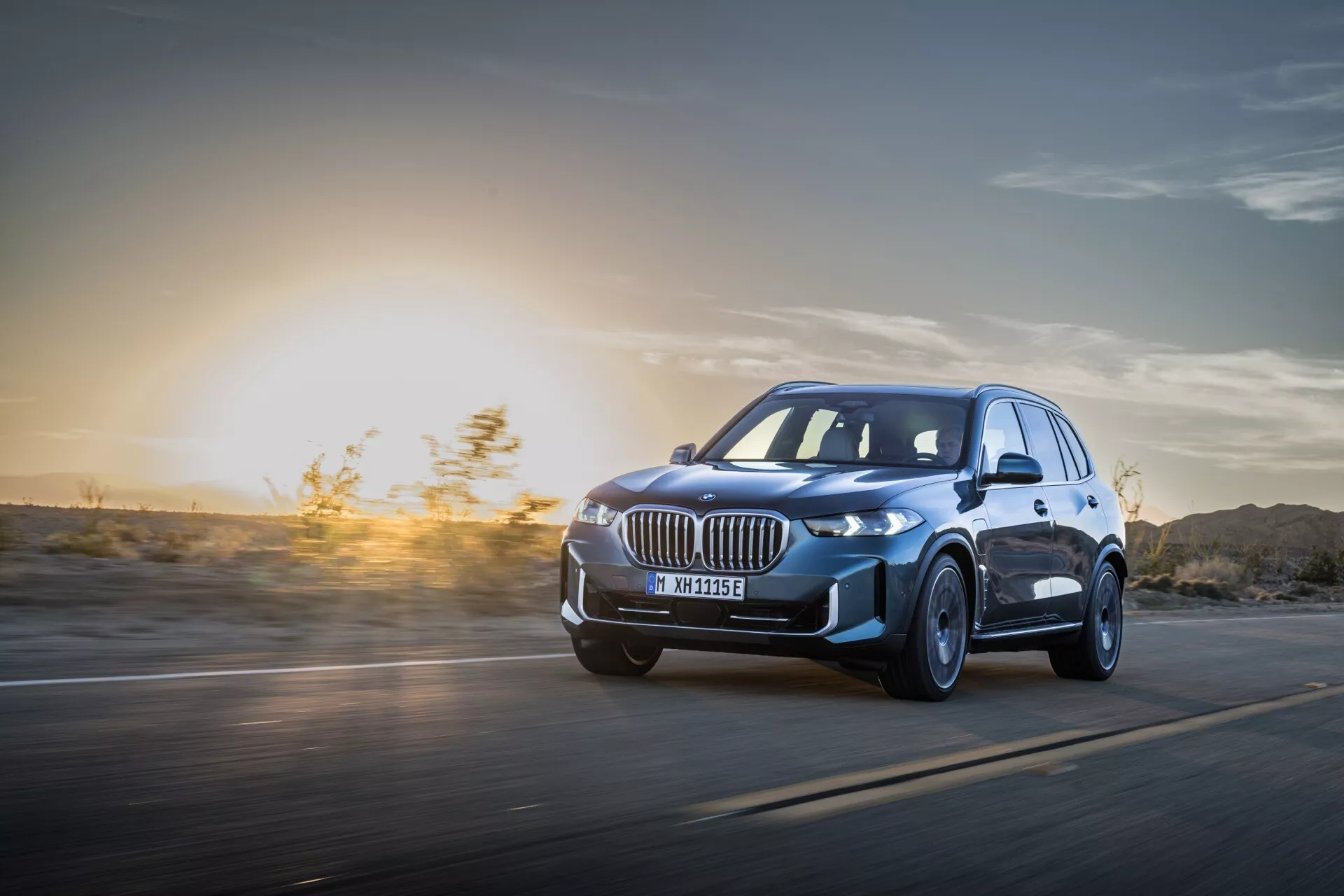 BMW X5 2023 (G05-F95 Facelift) w Ruchu: Dynamiczny Obraz z Niskiej Perspektywy Podkreślający Reflektory LED, Felgi ze Stopu i Aerodynamiczną Konstrukcję na Tle Zachodu Słońca