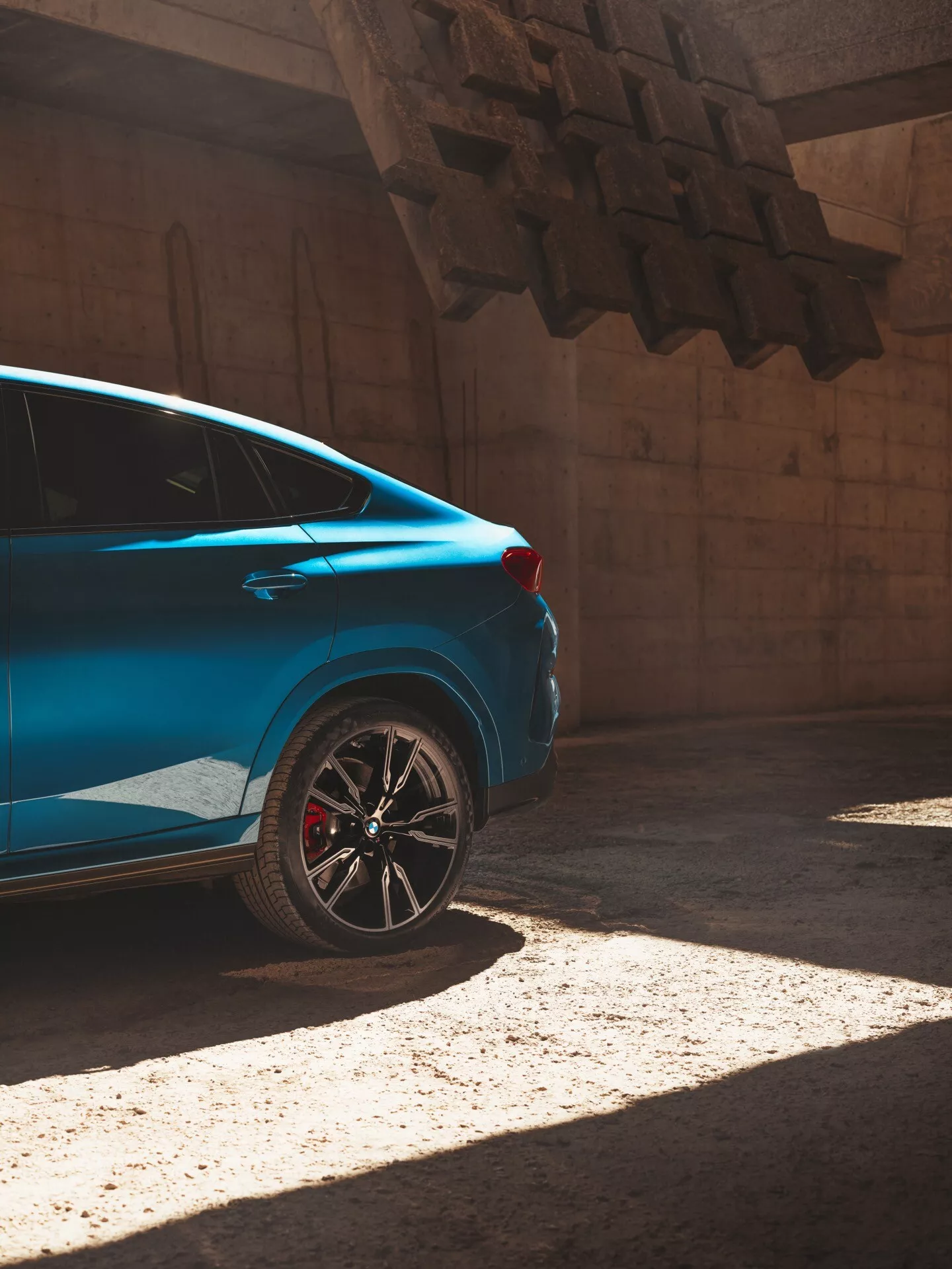 Niebieski samochód BMW X6 2023 (G06/F96 lifting) na słońcu, widziany z perspektywy trzech czwartych od tyłu, podkreślający tylną ćwiartkę z sportowym obręczem i czerwonym zaciskiem hamulcowym.