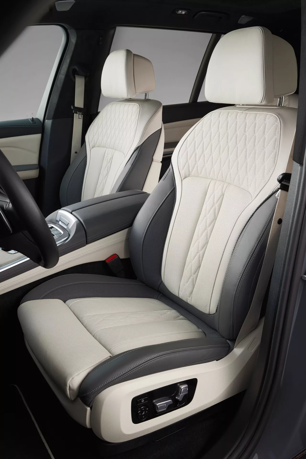 Szczegółowy widok wnętrza BMW X7 2022 (G07-facelift), skupiający się na ekskluzywnym, dwukolorowym skórzanym siedzeniu pasażera z pikowaniem w romby, elektroniczną regulacją, pasującym do luksusowego wzornictwa drzwi i konsoli środkowej