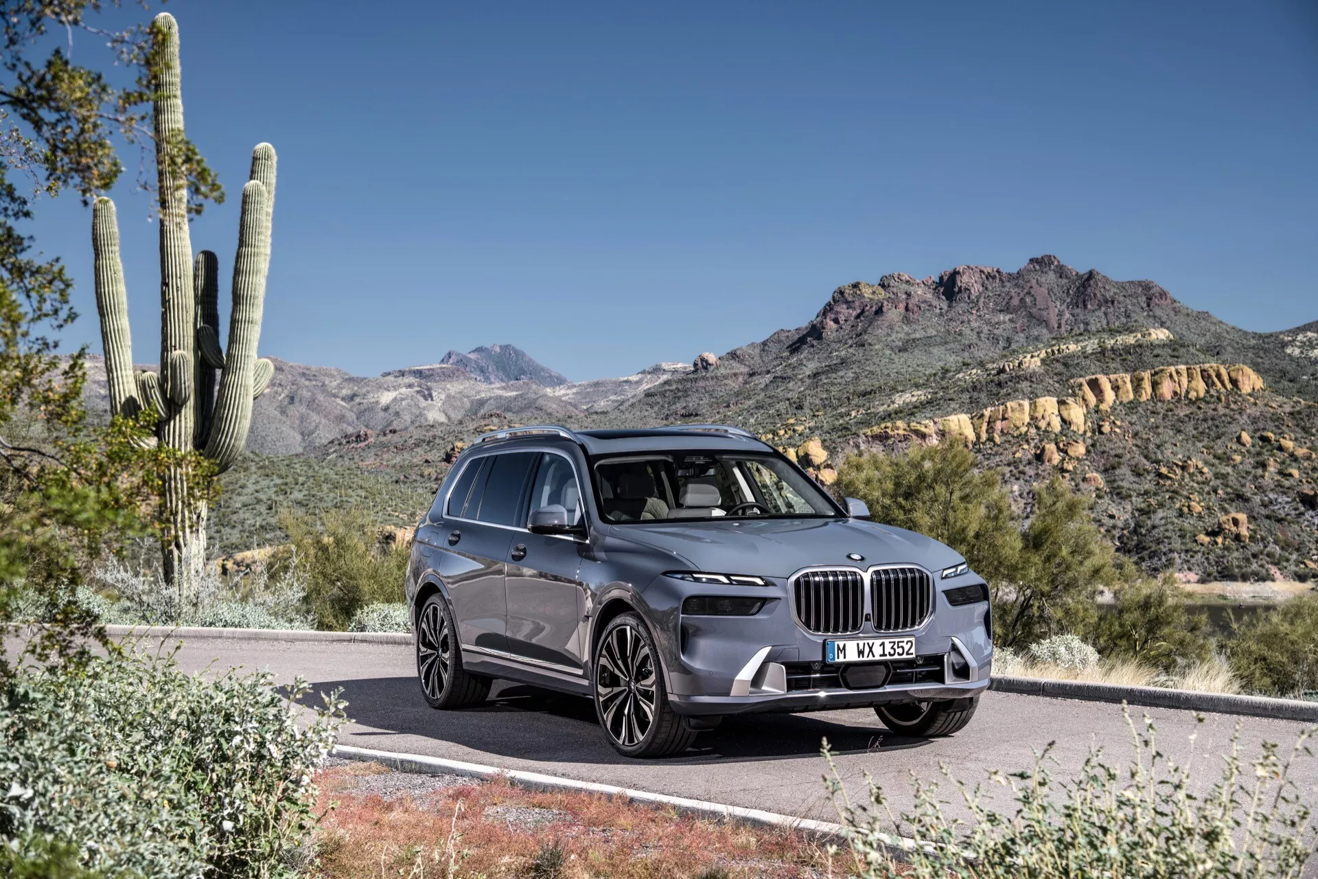 Widok z przodu trzy czwarte BMW X7 2022 (G07-Facelift) na utwardzonej drodze, prezentujący jego obszerną nerke grille, kątowe reflektory LED, profilowaną maskę i stronę kierowcy na tle pustyni i gór w świetle dziennym.