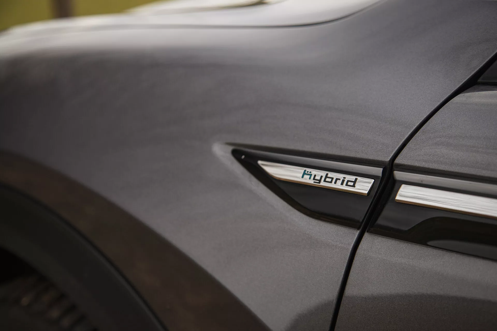 Zbliżenie szczegółu Citroen C5-X 2022 z emblematem Hybryda na dolnym bocznym profilu przy tylnym kole, prezentujące technologię hybrydową i estetykę projektowania w miękkich warunkach oświetleniowych