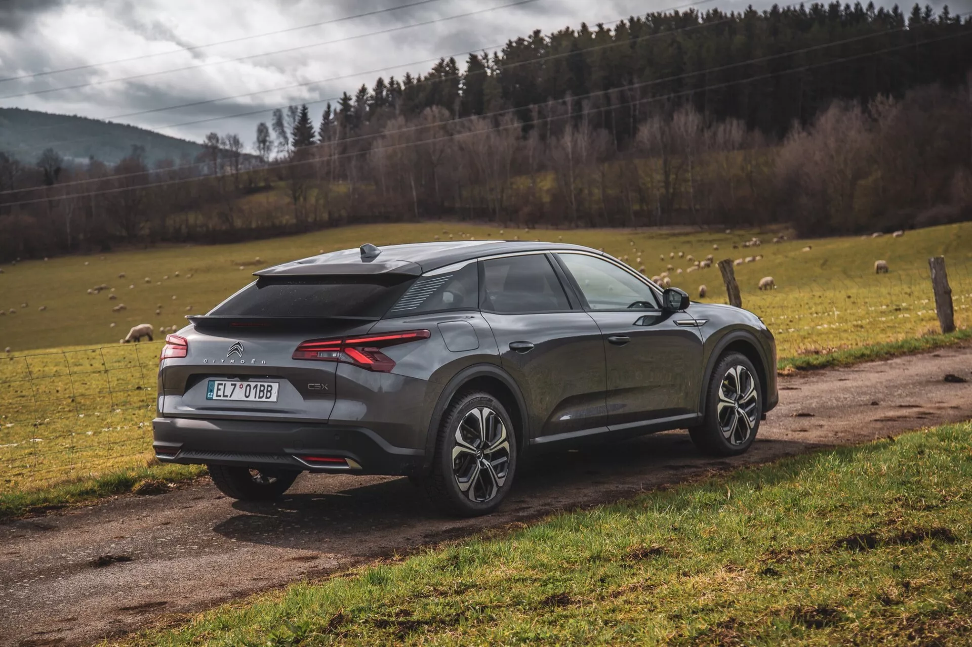 Nowoczesny SUV crossover Citroen C5-X 2022 zaparkowany na zewnątrz, widok z tyłu trzy czwarte podkreślający tylne światła LED, dyfuzor tylny, czujniki parkowania lub kamerę, antenę w kształcie płetwy rekina, dwukolorowe koła ze stopu, pochylone tylne okno, zintegrowany spoiler i metaliczne wykończenie na tle krajobrazu naturalnego