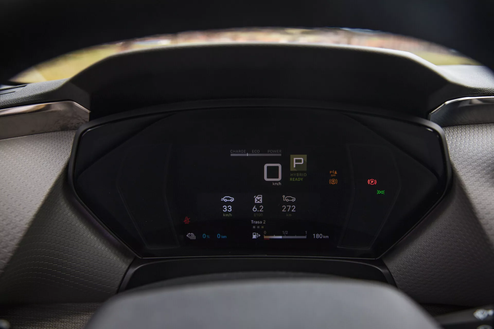 Zbliżony widok na cyfrowy desce rozdzielczej Citroen C5-X 2022 wyświetlający metryki pojazdu, w tym wskaźnik biegu, prędkościomierz i zużycie energii, z rozmytą kierownicą i przednią szybą na pierwszym planie i tle odpowiednio.