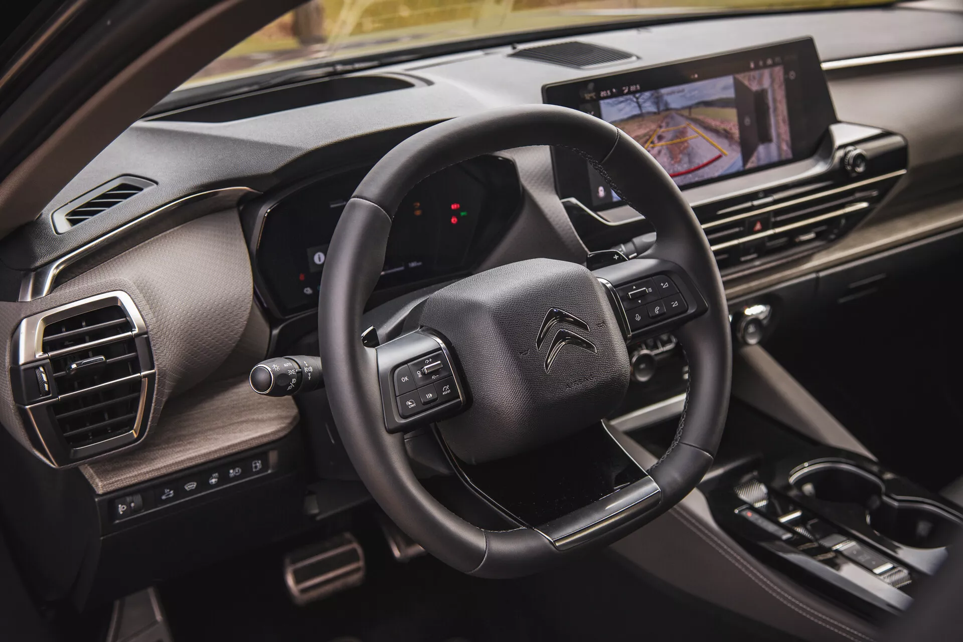 Zbliżony widok wnętrza Citroëna C5-X 2022, przedstawiający kierownicę z przyciskami wielofunkcyjnymi, cyfrową tablicę rozdzielczą z perspektywy pasażera oraz system infotainment z ekranem dotykowym