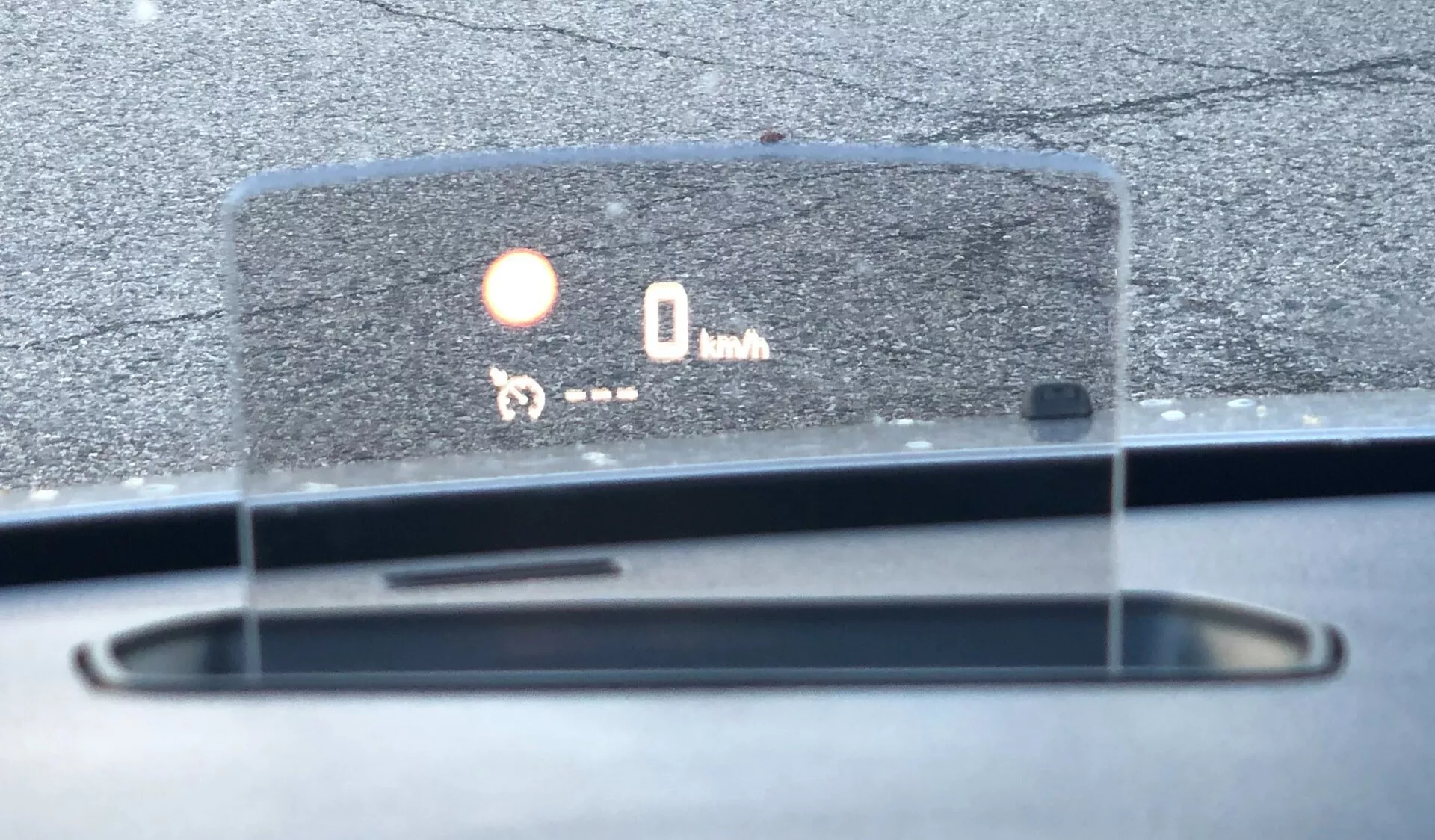 Zbliżenie wyświetlacza head-up (HUD) Citroena Spacetourer 2016 rzutującego informacje na przednią szybę, pokazującego prędkość (0 km/h) i ikonę, prawdopodobnie wskazującą czujnik parkowania lub system ostrzegania przed kolizją. Szczegóły deski rozdzielczej, wyloty odmrażania, odbicie światła słonecznego sugerują dzienne ustawienie na zewnątrz. Kąt pokazuje perspektywę kierowcy, koncentrując się na HUD.