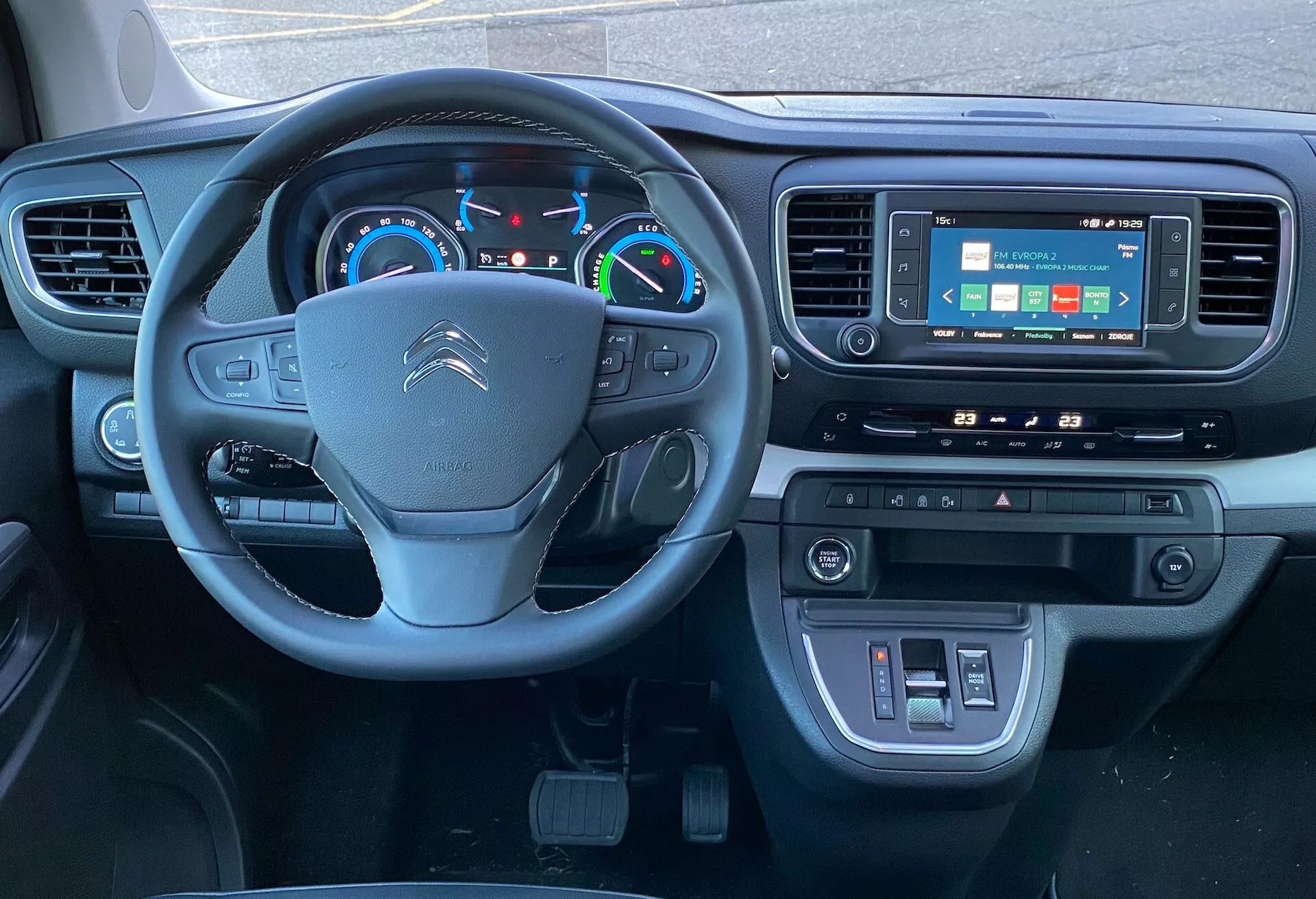 Widok wnętrza Citroëna SpaceTourer 2016 z perspektywy fotela kierowcy, ukazujący kierownicę z wielofunkcyjnymi przyciskami, cyfrowy zestaw wskaźników oraz umieszczony centralnie system infotainment z ekranem dotykowym, a także sterowanie klimatyzacją i łączność USB poniżej. Nacisk na technologię i nowoczesny design.