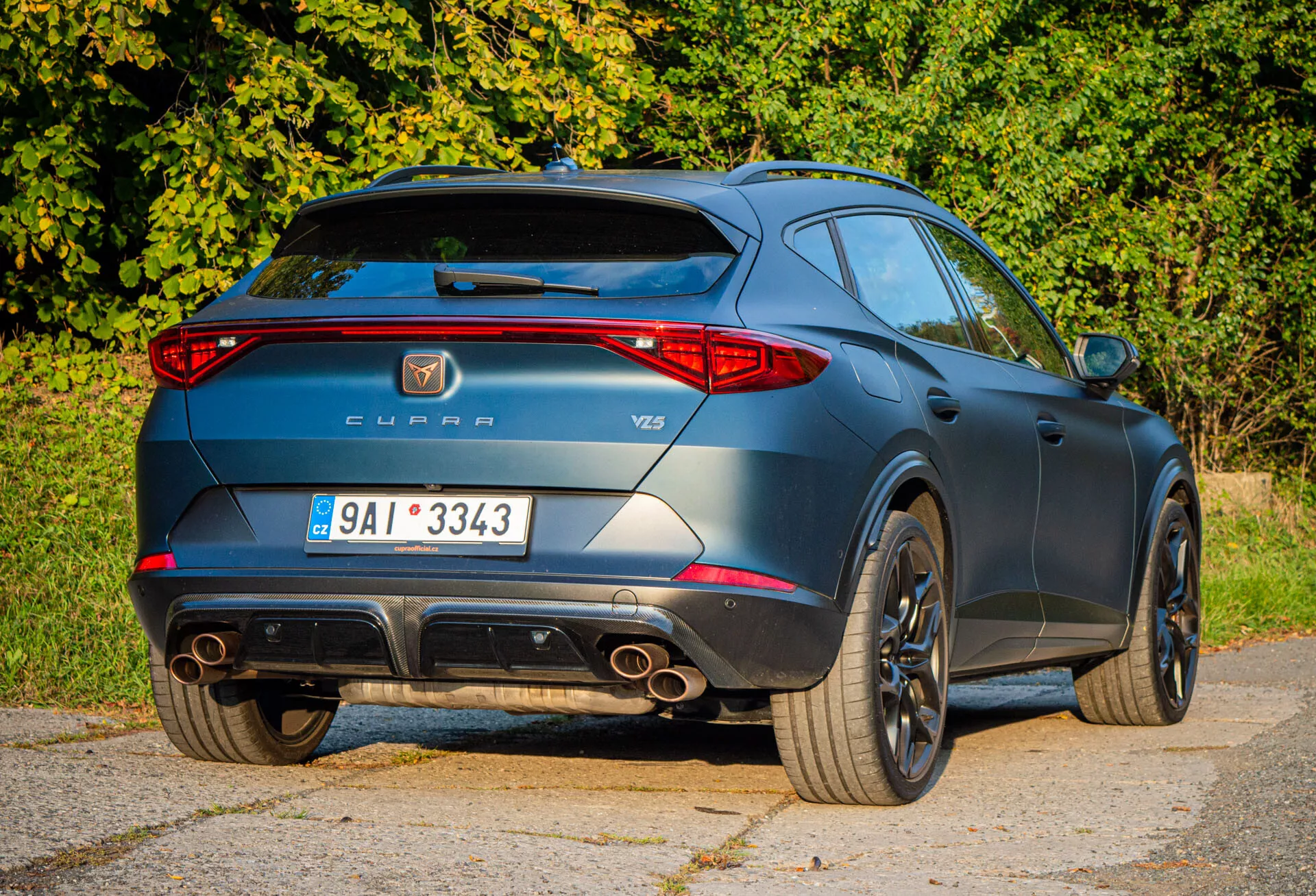 Tylny widok z ujęciem trzech czwartych Cupra Formentor 2020, podkreślający sportowe cechy takie jak podwójne końcówki wydechu, spojler dachowy i koła ze stopów, wraz z oznaczeniami producenta i modelu w ciągu dnia