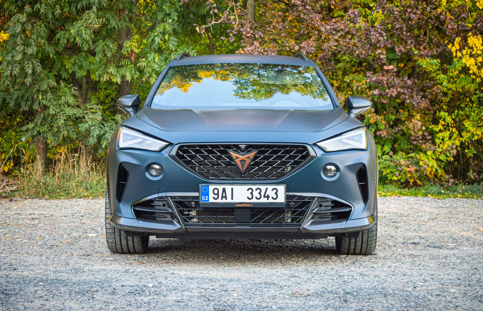 Widok z przodu Cupra Formentor 2020 prezentujący nowoczesny design, dużą atrapę z emblematem, geometryczny wzór atrapy, smukłe reflektory LED, światła przeciwmgielne, sportowy przedni zderzak z dużymi wlotami powietrza, charakterystyczne linie na masce, centralną europejską tablicę rejestracyjną oraz spoiler dolny poprawiający aerodynamikę.