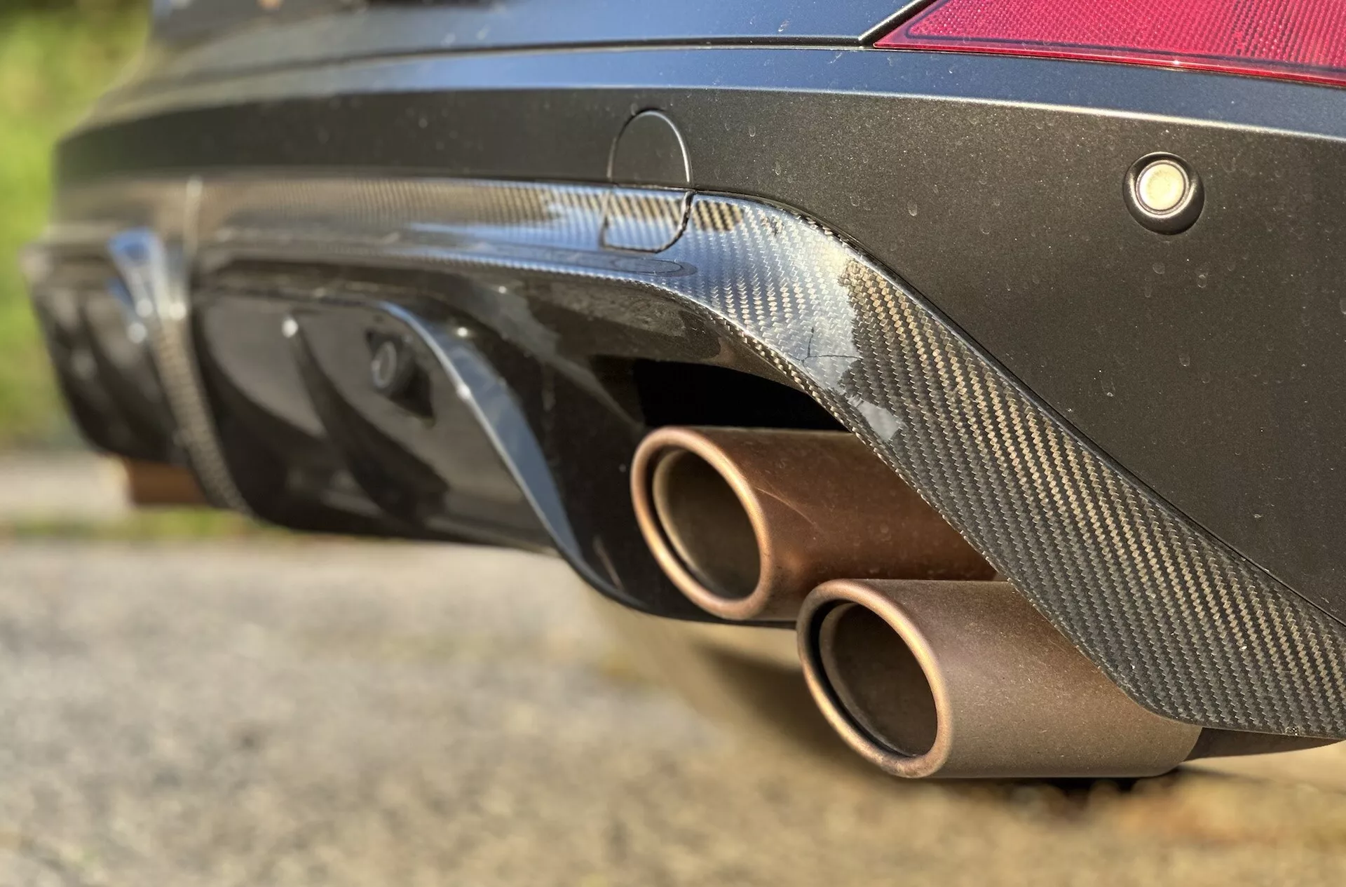 Zbliżenie na tylną część Cupra Formentor 2020, prezentujące brązowe rury wydechowe, dyfuzor z włókna węglowego, system czujników i czarny kolor nadwozia z niskiej perspektywy podkreślające jego sportowy design i cechy wydajności