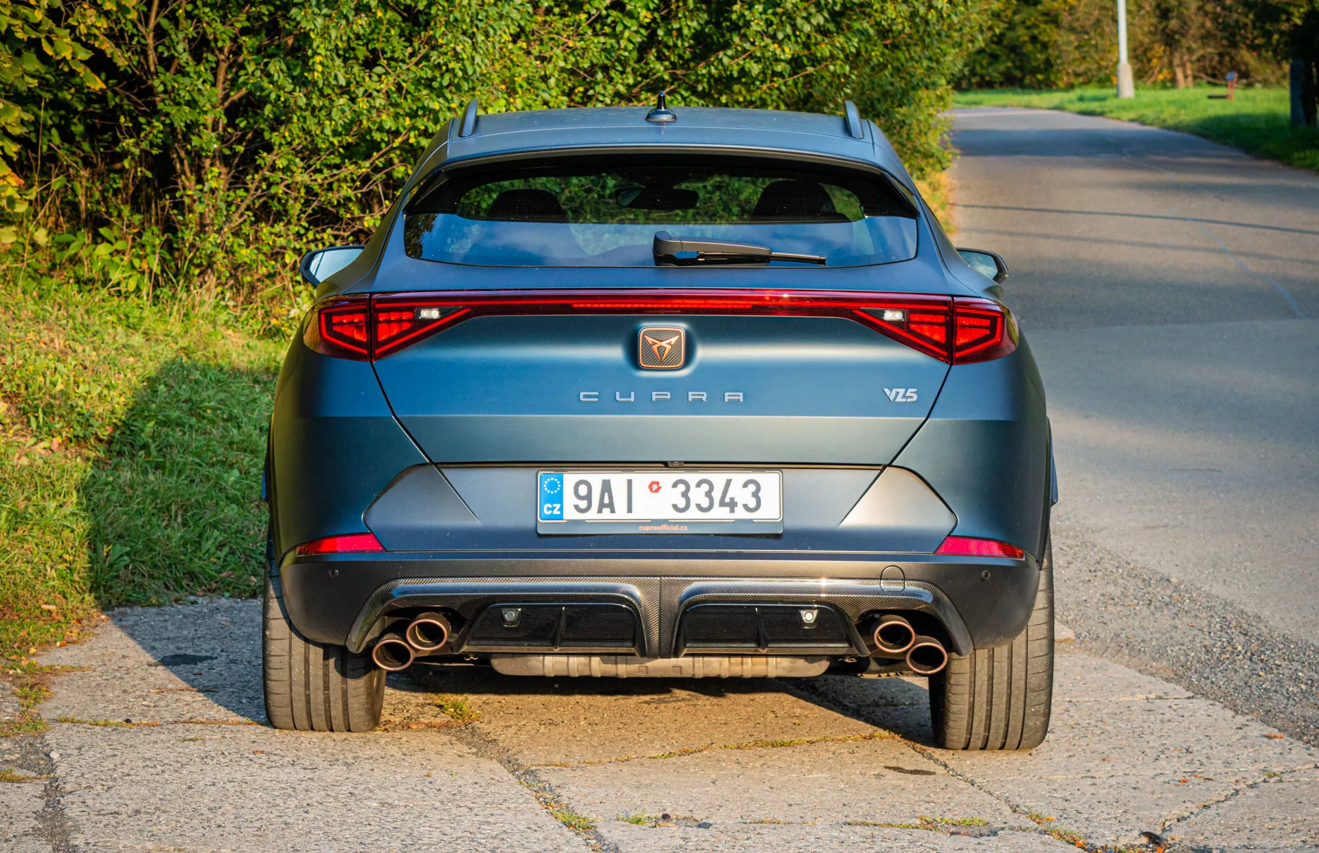 Tylny widok metalicznie szarego CUPRA Formentor VZ5 z 2020 roku zaparkowanego przy drodze, prezentujący LED-owe światła tylne, podwójne rury wydechowe i aerodynamiczne cechy konstrukcyjne podczas zdjęcia w świetle dzienne późnym popołudniem