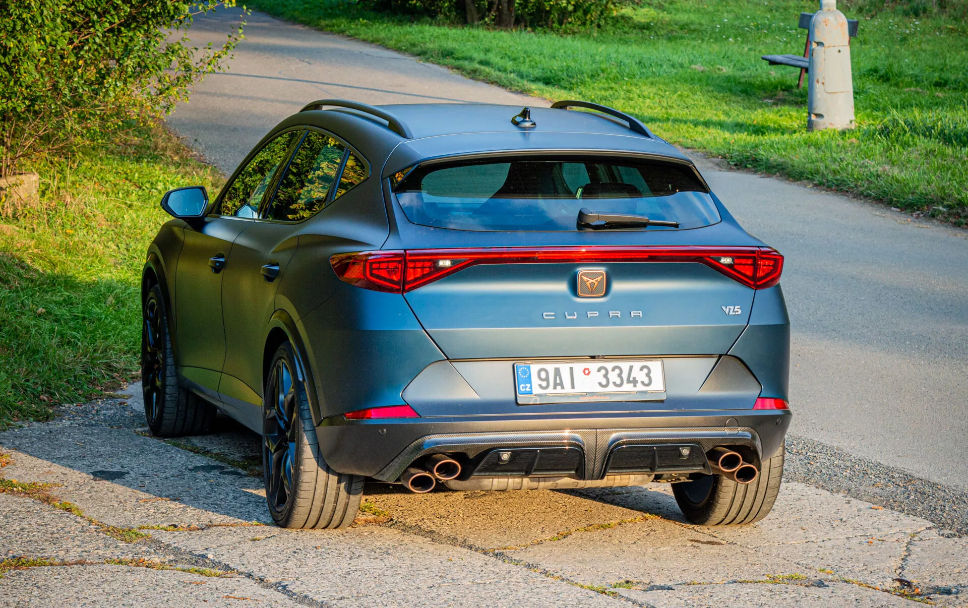 Widok tylny SUV Cupra Formentor VZ5 2020 z tylnymi światłami LED, czterorurkowym systemem wydechowym, sportowym dyfuzorem i zderzakiem, kołami wieloramieniowymi i matowym wykończeniem w kolorze antracyt, sfotografowany w scenerii podmiejskiej w świetle dziennym