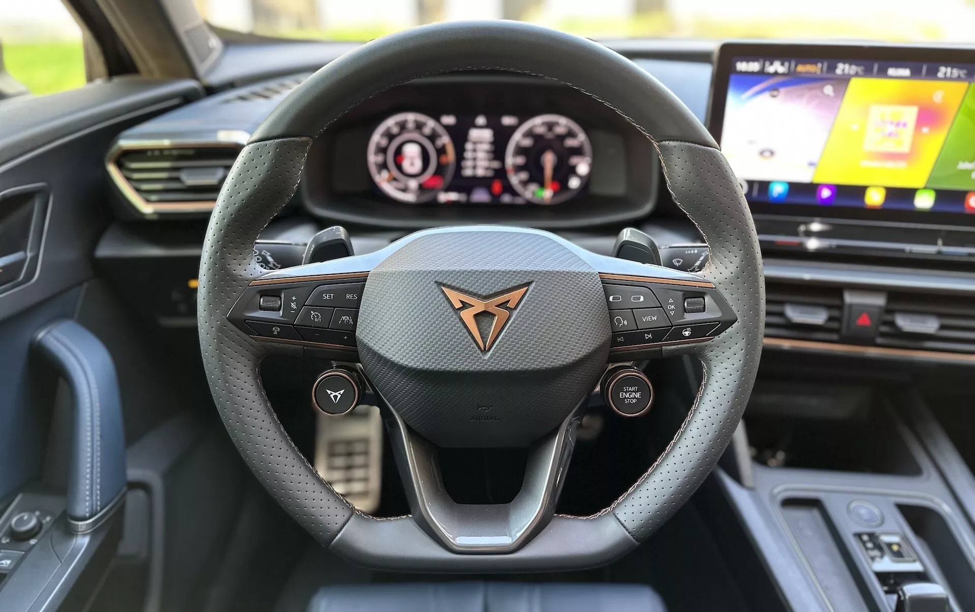 Widok wnętrza Cupra Formentor 2020 z perspektywy miejsca kierowcy, podkreślający kierownicę o trójramiennym wzorze obszytą skórą z przyciskami wielofunkcyjnymi, cyfrowy panel zegarów i system infotainment z ekranem dotykowym.