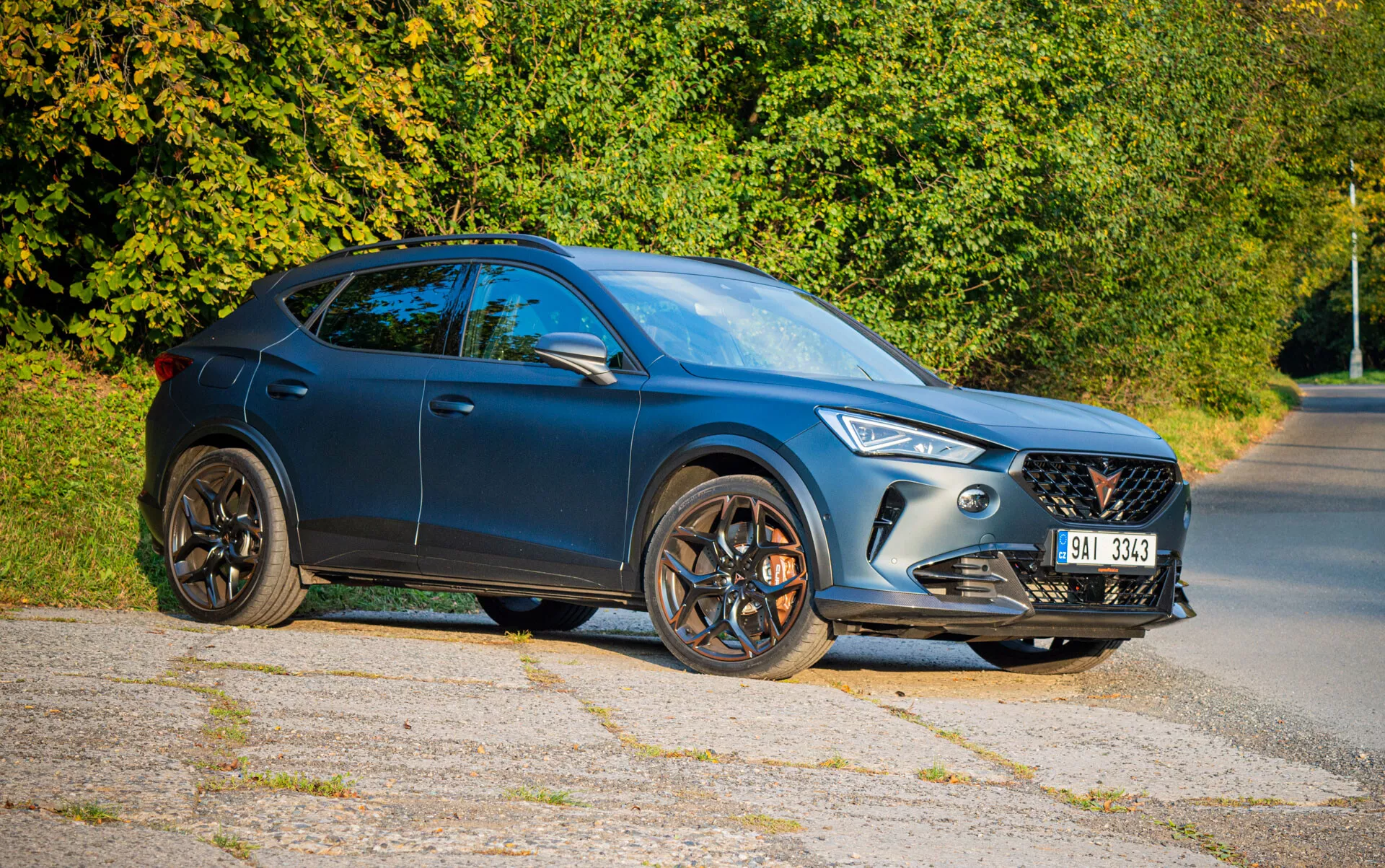 Crossover SUV Cupra Formentor 2020 w ciemnoniebieskim kolorze, z eleganckim designem, światłami LED i pięcioramienne koła ze stopu, sfotografowany z przodu z perspektywy trzech czwartych na przedmieścia