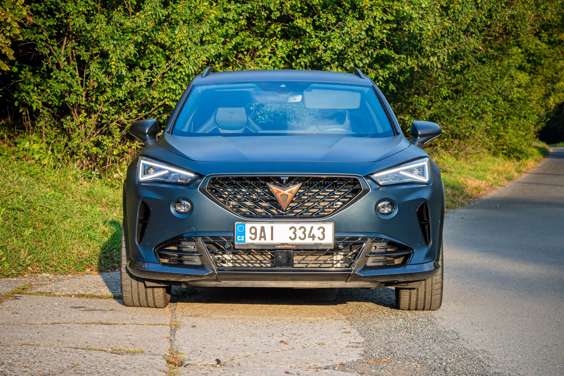 Nowoczesny, przedni widok Cupra Formentor 2020 na utwardzonej drodze przy naturalnym świetle dziennym i wiejskim tle, podkreślający agresywną atrapę, ostre reflektory LED, dynamiczne linie maski i zaawansowane funkcje technologiczne