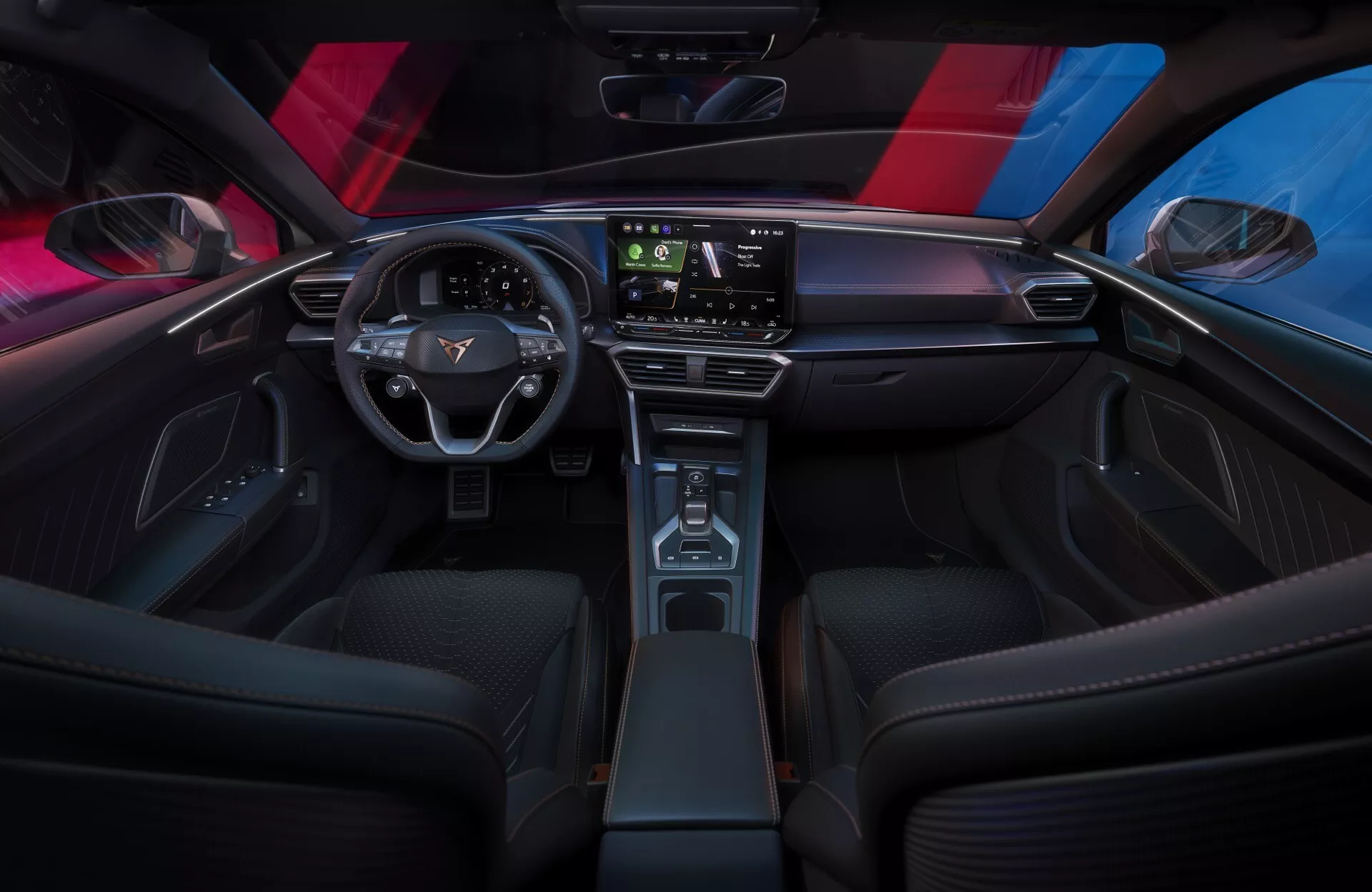 Wnętrze Cupra Leon 2024 (lifting pierwszej generacji) z perspektywy tylnego siedzenia, ukazujące elegancką, minimalistyczną deskę rozdzielczą z dużym ekranem dotykowym, nowoczesną dwuramienną kierownicę z kontrolkami pojazdu oraz wąską konsolę środkową z drewnianymi wykończeniami. Sportowe przednie siedzenia, oświetlenie ambientowe i panoramiczny dach podkreślają wyrafinowaną, technologiczną atmosferę wnętrza.