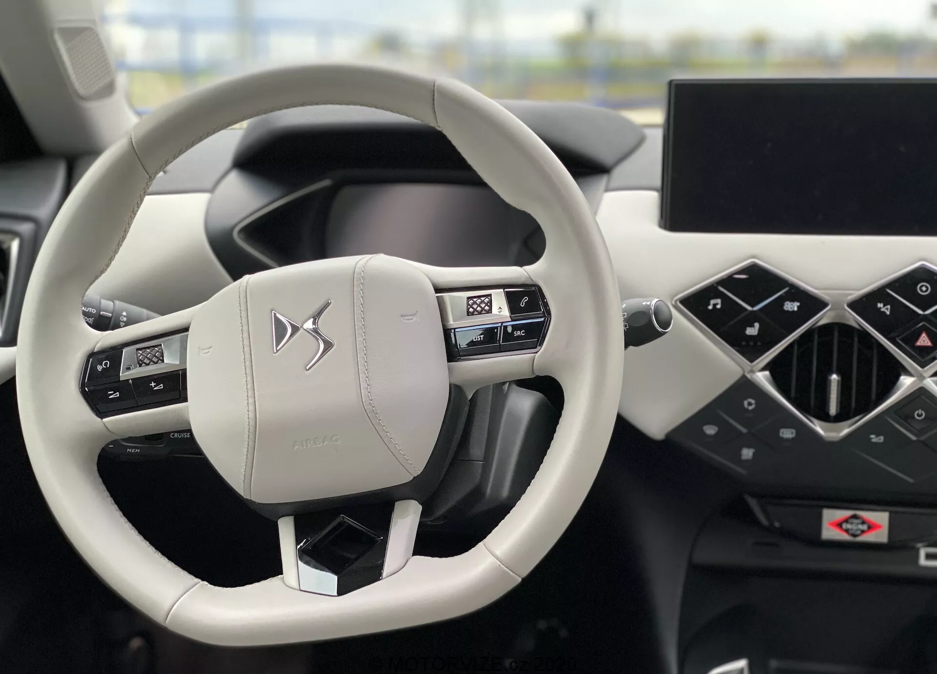 Widok wnętrza DS Automobiles DS-3 Crossback E-Tense 2019 koncentrujący się na kierownicy i desce rozdzielczej z perspektywy kierowcy. Dwuramienna kierownica, obszyta skórą z przeszyciami, zawiera zintegrowane przyciski do obsługi dźwięku, telefonu i ustawień pojazdu. Deska rozdzielcza wyposażona jest w cyfrowy zestaw wskaźników oraz duży poziomy ekran systemu infotainment. Minimalistyczny, nowoczesny design i wysokiej jakości materiały podkreślają luksusowy charakter pojazdu.