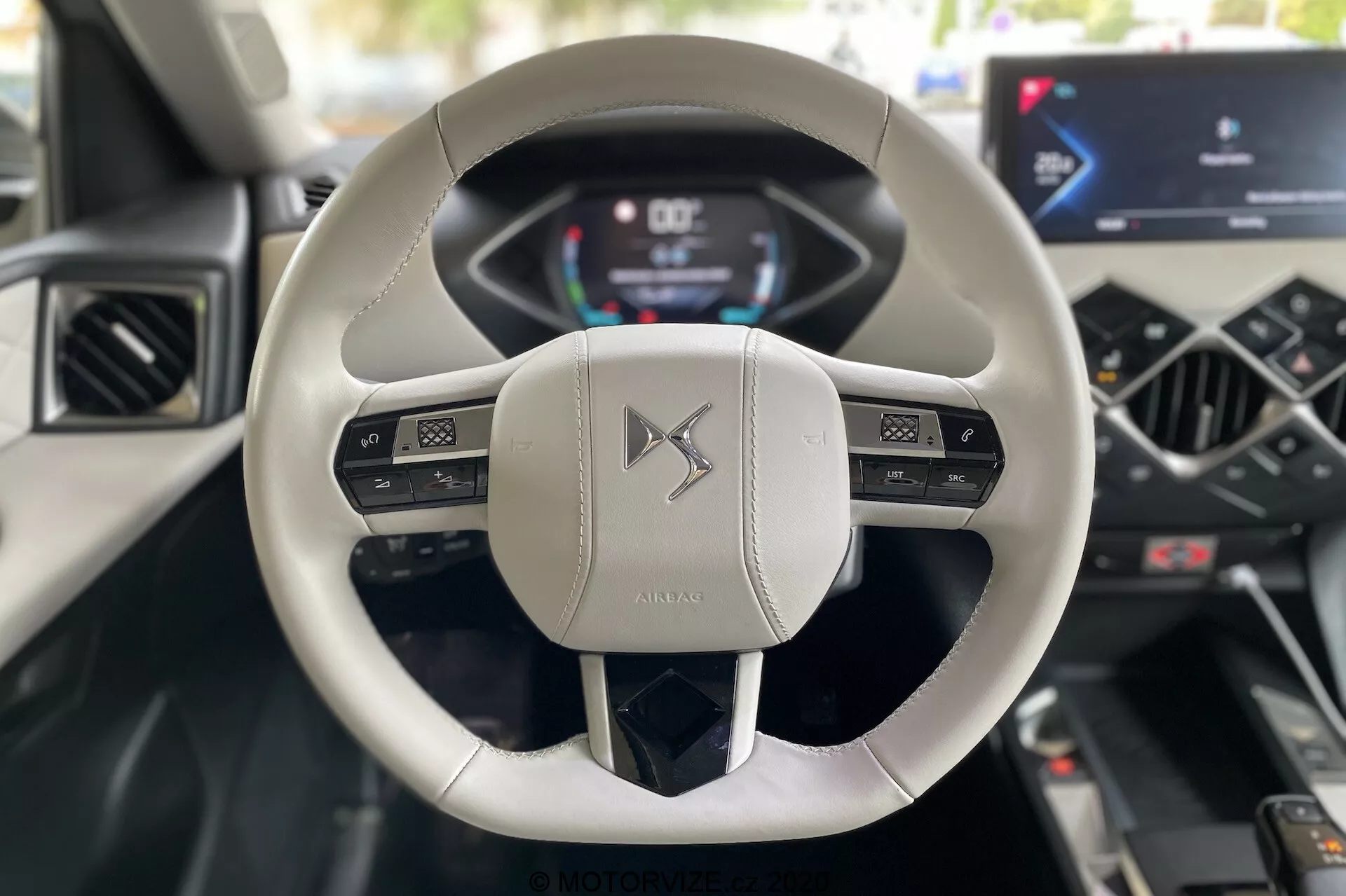Widok wnętrza z perspektywy kierowcy w DS Automobiles DS 3 Crossback E-Tense 2019, ze szczególnym uwzględnieniem nowoczesnej, dwuramiennej kierownicy pokrytej jasną skórą, posiadającej wielofunkcyjne przyciski oraz cyfrowego zestawu wskaźników wyświetlającego prędkość i obroty. Konsola centralna wyposażona jest w zintegrowany dotykowy ekran infotainmentu i minimalistyczne elementy sterowania klimatyzacją, podkreślające zaawansowaną technologię motoryzacyjną i luksusowy design.