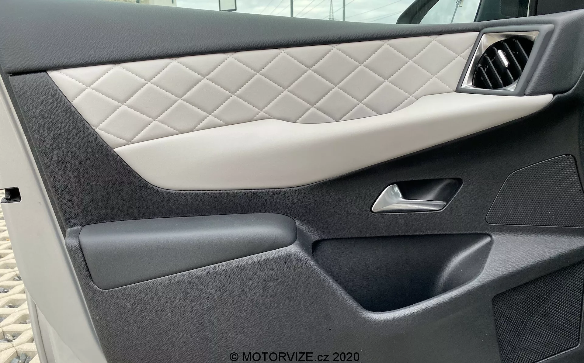 Zbliżenie na wewnętrzny panel drzwi pojazdu DS Automobiles DS-3 2019 (DS-3-Crossback-E-Tense), prezentujący pikowane tapicerstwo z wzorem w romby, elegancki srebrny uchwyt, ciemne sekcje wysokiej jakości plastiku o różnorodnych teksturach oraz bezszwową dolną kieszeń na przechowywanie, podkreślając luksusowy i szczegółowy design samochodu.