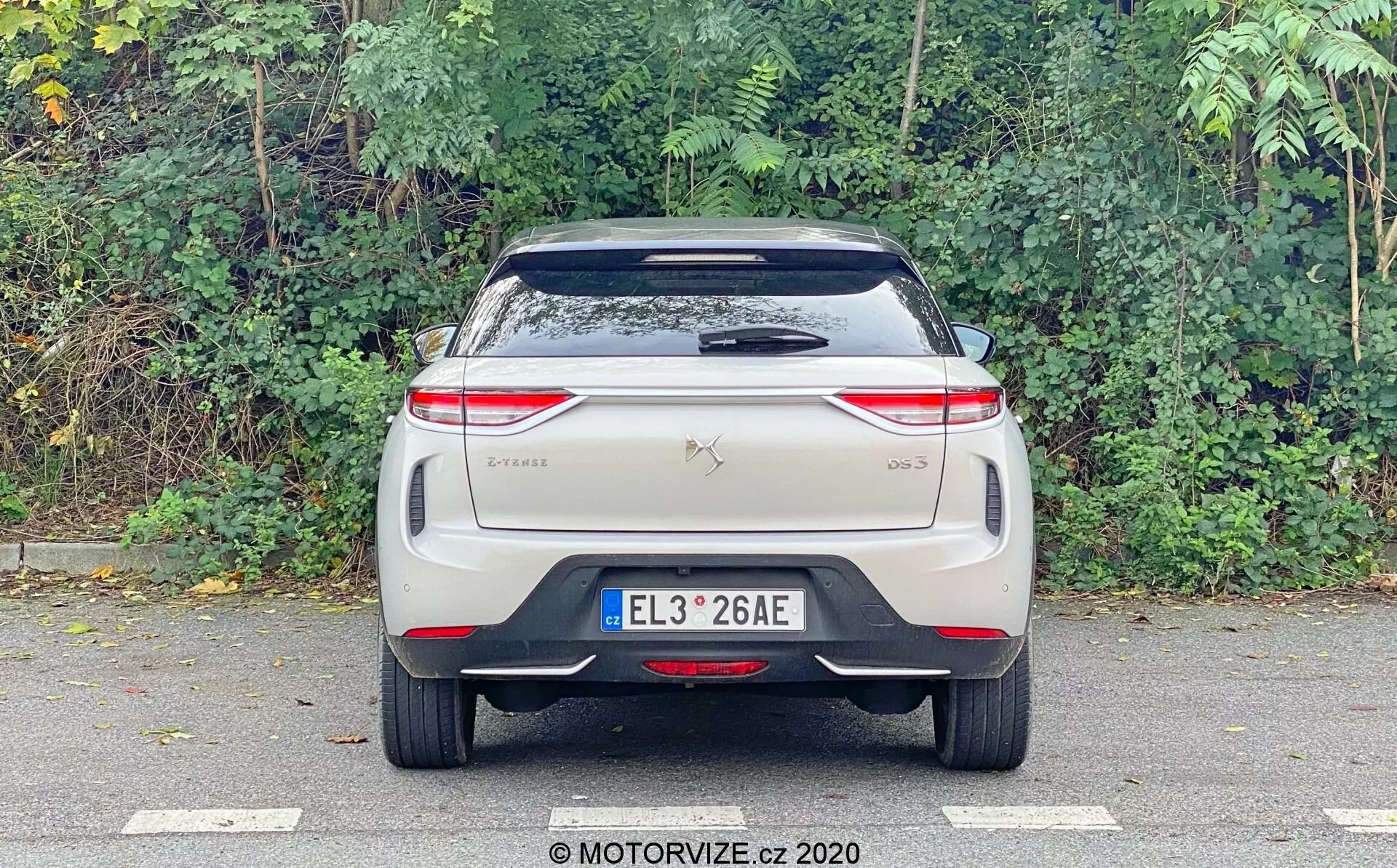 Obraz pokazuje widok tylu samochodu DS Automobiles DS 3 Crossback E-Tense z 2019 roku, sfotografowanego na wysokości oczu z naciskiem na tylną część. Widoczne elementy to centralnie umieszczona tablica rejestracyjna, odznaki marki i modelu na klapie bagażnika, nowoczesne poziome światła tylne z złożonymi wzorami LED, tylna szyba z wycieraczką, spoiler dachowy i zderzak z odblaskowym paskiem. Brak tradycyjnych końcówek wydechu sugeruje, że jest to pojazd elektryczny. Design jest czysty, prawdopodobnie zawierający zaawansowane funkcje technologiczne typowe dla samochodów elektrycznych lub hybrydowych.