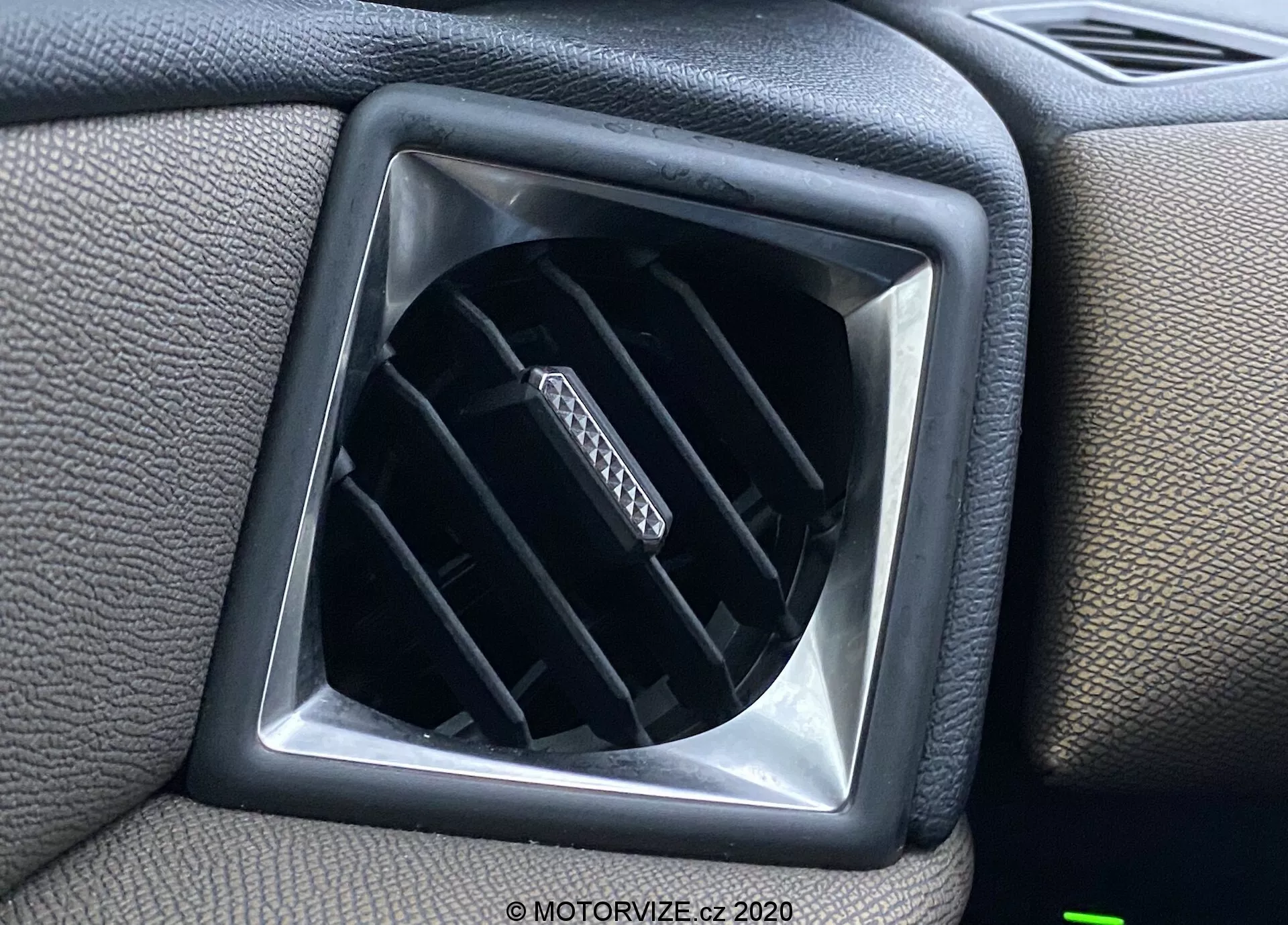 Zbliżenie na kratkę wentylacyjną wewnątrz pojazdu DS Automobiles DS-3 Crossback 2019, ukazującą regulowane poziome łopatki w otworze o kształcie diamentu, otoczone powierzchnią deski rozdzielczej z teksturowanego plastiku z kwadratową ramką dla dodatkowego elementu designu.