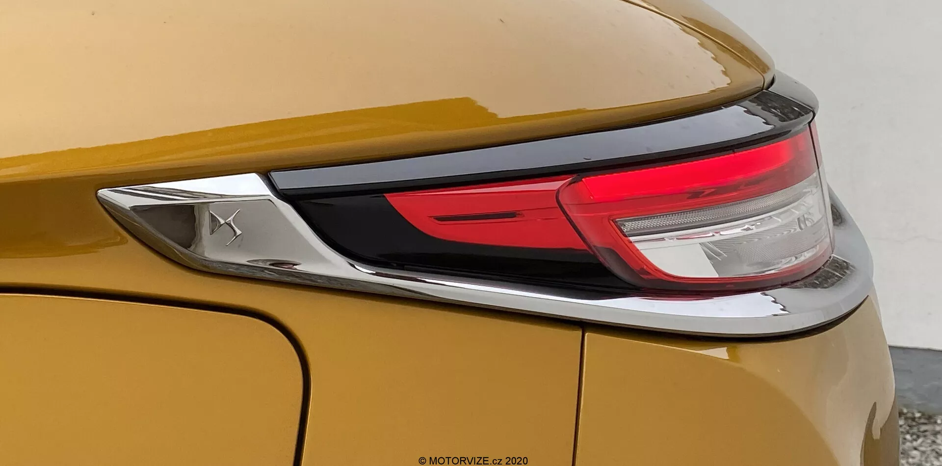 Zbliżony widok tylnej części samochodu DS Automobiles DS-3 2019 (DS-3 Crossback). Obraz skupia się na prawej stronie pojazdu, prezentując metaliczne złote lub brązowe nadwozie, część zestawu tylnego światła LED i gładki, zaokrąglony tylny kwatery z wyraźną linią charakteru. Widać także chromowany emblemat, ale nie ujawnia on marki.