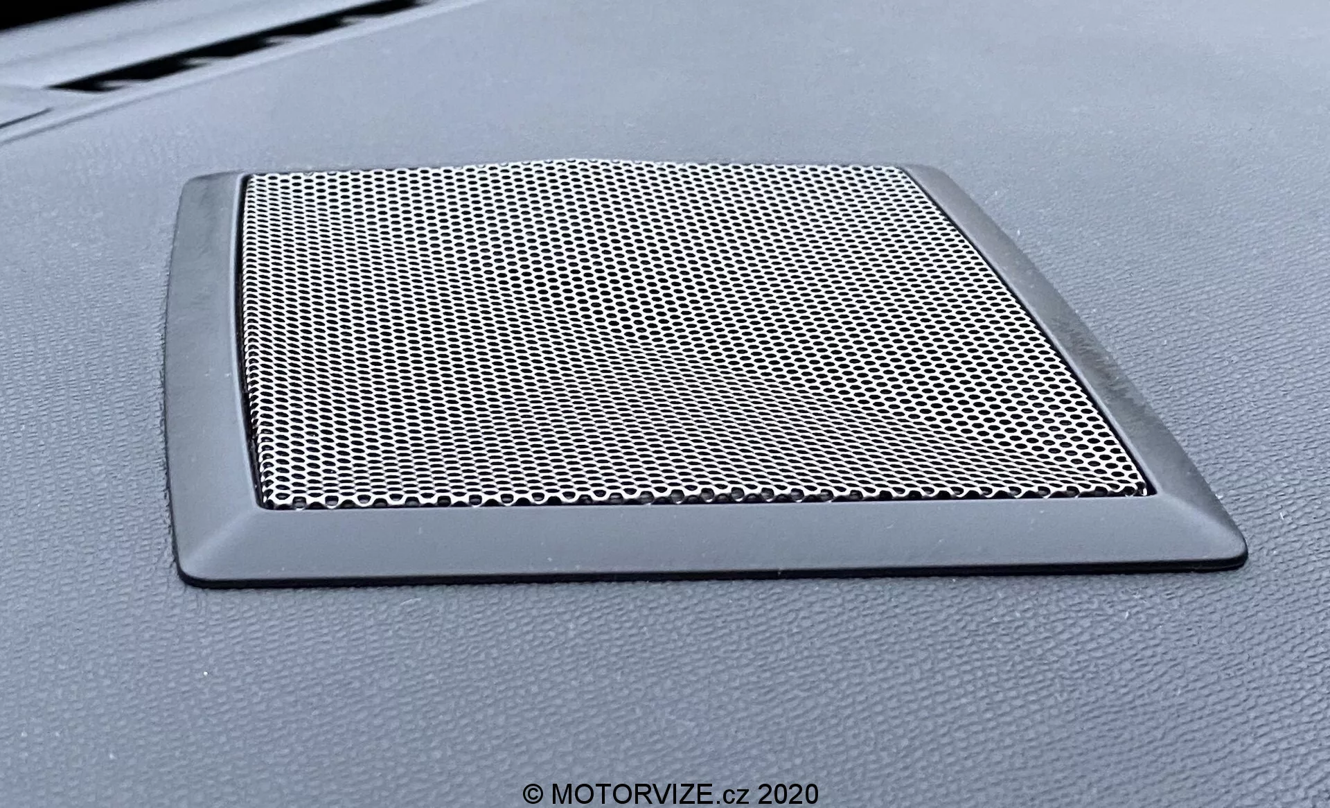 Zbliżenie na kratkę głośnika na desce rozdzielczej pojazdu DS Automobiles DS-3 Crossback model 2019. Kratka trapezoidalna z gęstą siatką chroniącą głośnik i eleganckim, nierefektywnym brzegiem, który harmonizuje z deską rozdzielczą.