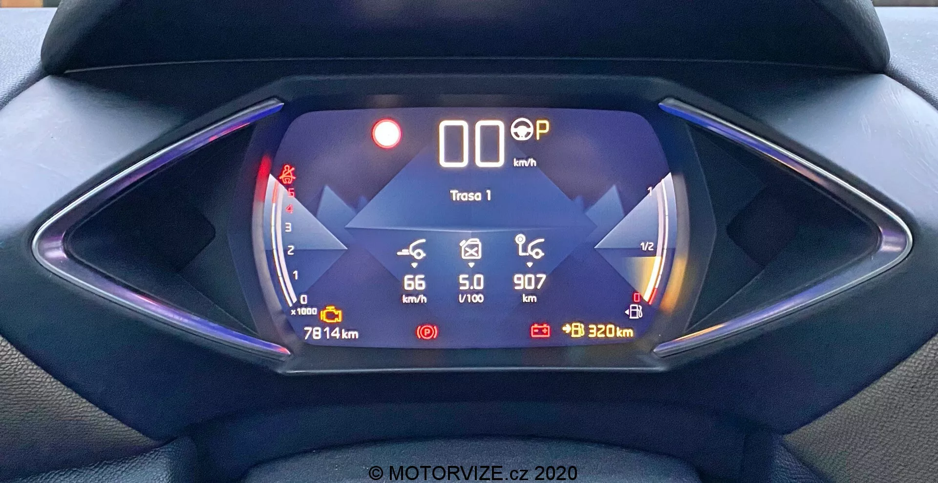 Cyfrowa deska rozdzielcza DS Automobiles DS-3 2019 (DS-3 Crossback) widziana z perspektywy kierowcy. Symetryczna kompozycja skupiająca się na futurystycznym, sześciokątnym panelu instrumentów z cyfrowym wyświetlaczem zdominowanym przez niebieski kolor. Funkcje obejmują wskaźnik zasięgu baterii pokazujący '66 km' po lewej, prędkość '0 km/h' w środku, pozycję biegu 'P', ikonę śliskiej drogi i wskaźnik '320 m' po prawej. Dodatkowe dane obejmują temperaturę zewnętrzną '5,0°C', aktualny czas '9:07' i przebieg pojazdu '7814 km'. Obraz ten podkreśla cechy elektrycznego lub hybrydowego pojazdu z zaawansowaną technologią i cyfrowymi infografikami.