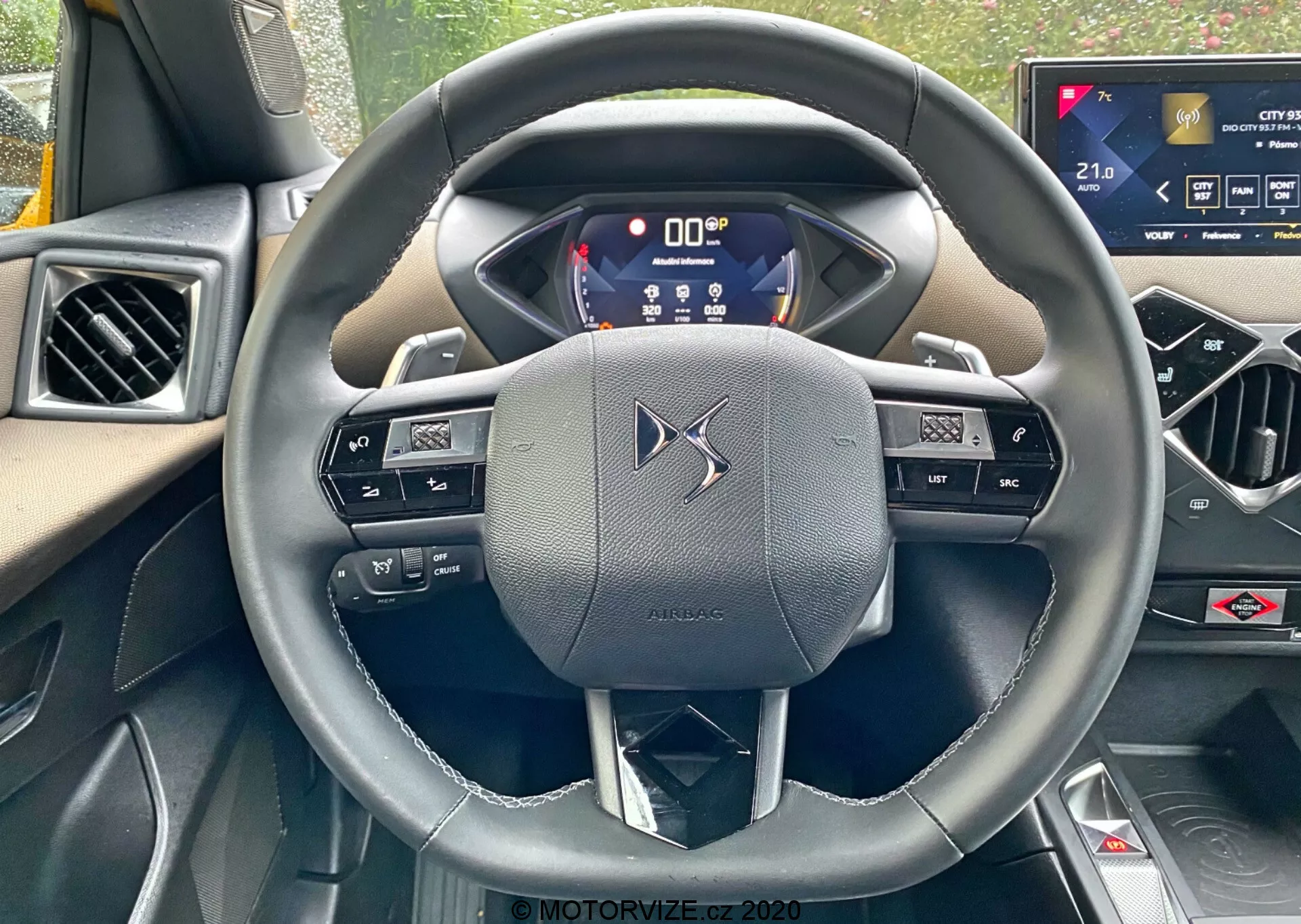Perspektywa pierwszoosobowa z miejsca kierowcy w DS-Automobiles DS-3 2019 (DS-3 Crossback), koncentrująca się na skórzanej, trójramiennej kierownicy ze zintegrowanymi przyciskami i łopatkami zmiany biegów. Cyfrowy panel instrumentów wyświetla kluczowe informacje, podkreślając zaawansowaną technologię pojazdu. Dotykowy system infotainment na konsoli środkowej sugeruje wysoki poziom funkcji wygodowych samochodu.