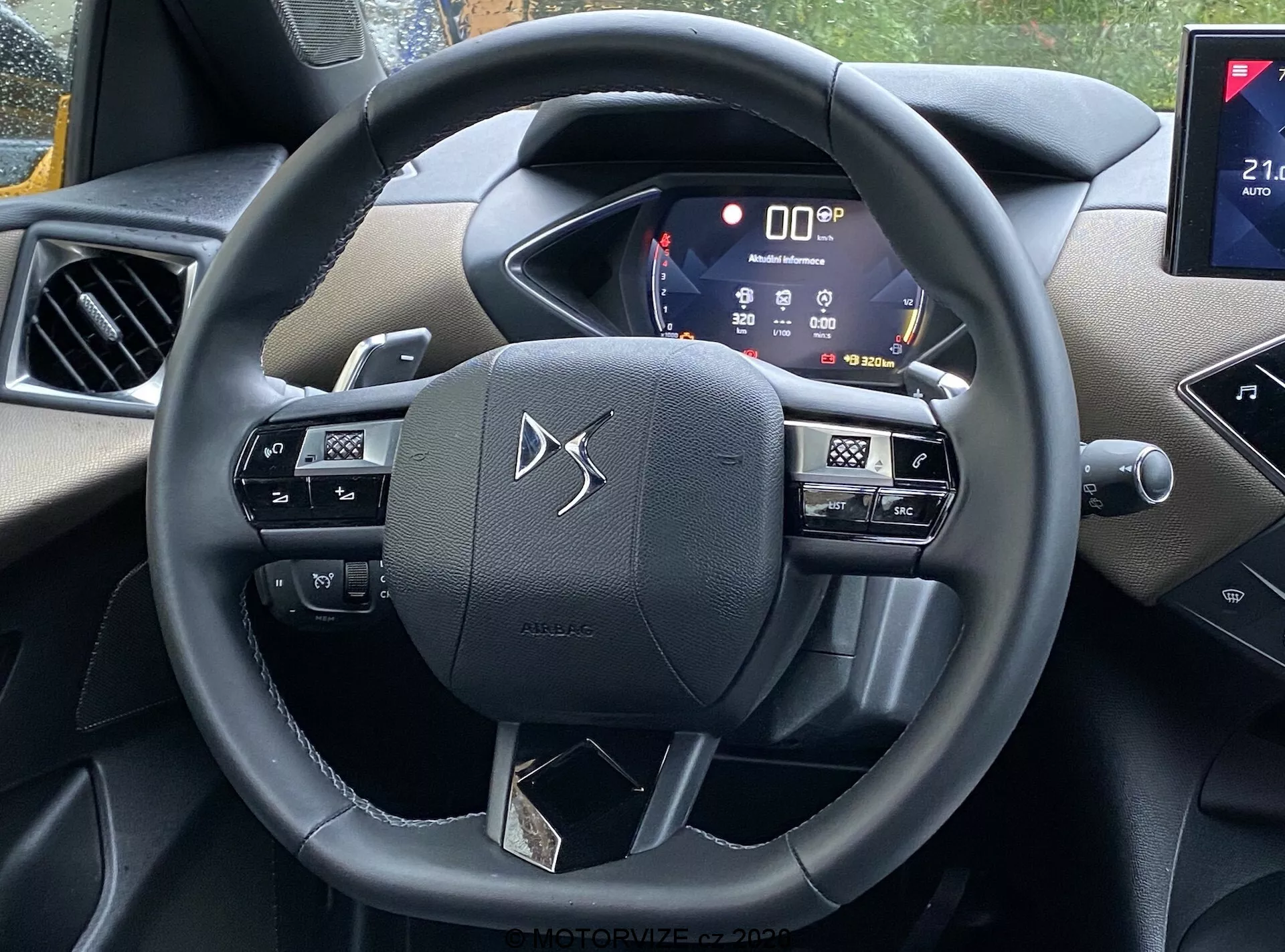Widok wnętrza samochodu DS Automobiles DS-3 2019 (DS-3 Crossback) z perspektywy siedzenia kierowcy, z kierownicą z przyciskami do sterowania multimediami, poleceniami głosowymi i prawdopodobnie ustawieniami tempomatu, aktywnym cyfrowym zestawem wskaźników pokazującym różne dane pojazdu i częścią systemu informacyjno-rozrywkowego z potencjalną łącznością ze smartfonami i funkcjami nawigacyjnymi. Wnętrze zawiera mieszankę miękkich plastikowych elementów i chromowanych akcentów, prezentując nowoczesną technologię oraz atrakcyjny wygląd.