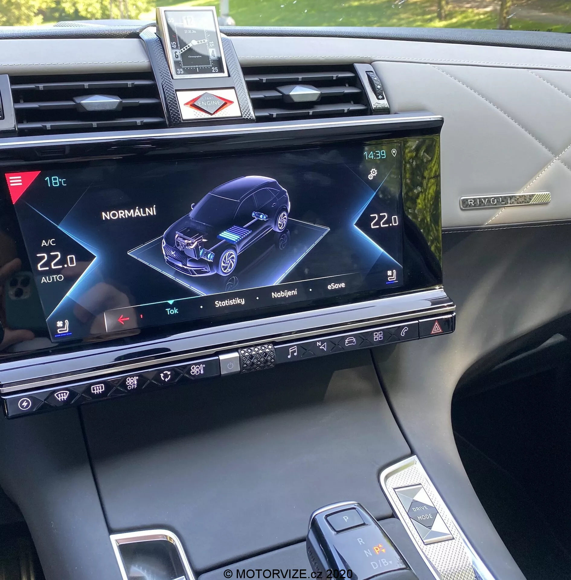 Konsola centralna DS Automobiles DS-7 Crossback 2018, pokazująca ekran systemu infotainment z graficzną reprezentacją 3D samochodu z perspektywy przednio-prawej, wskazującą stan i różne ustawienia, takie jak klimatyzacja, podgrzewanie siedzeń i interaktywne funkcje modelu samochodu, wraz z przyciskami fizycznymi, dotykowymi elementami sterującymi i częściowym widokiem na dźwignię zmiany biegów oraz pokrętło ustawień pojazdu.