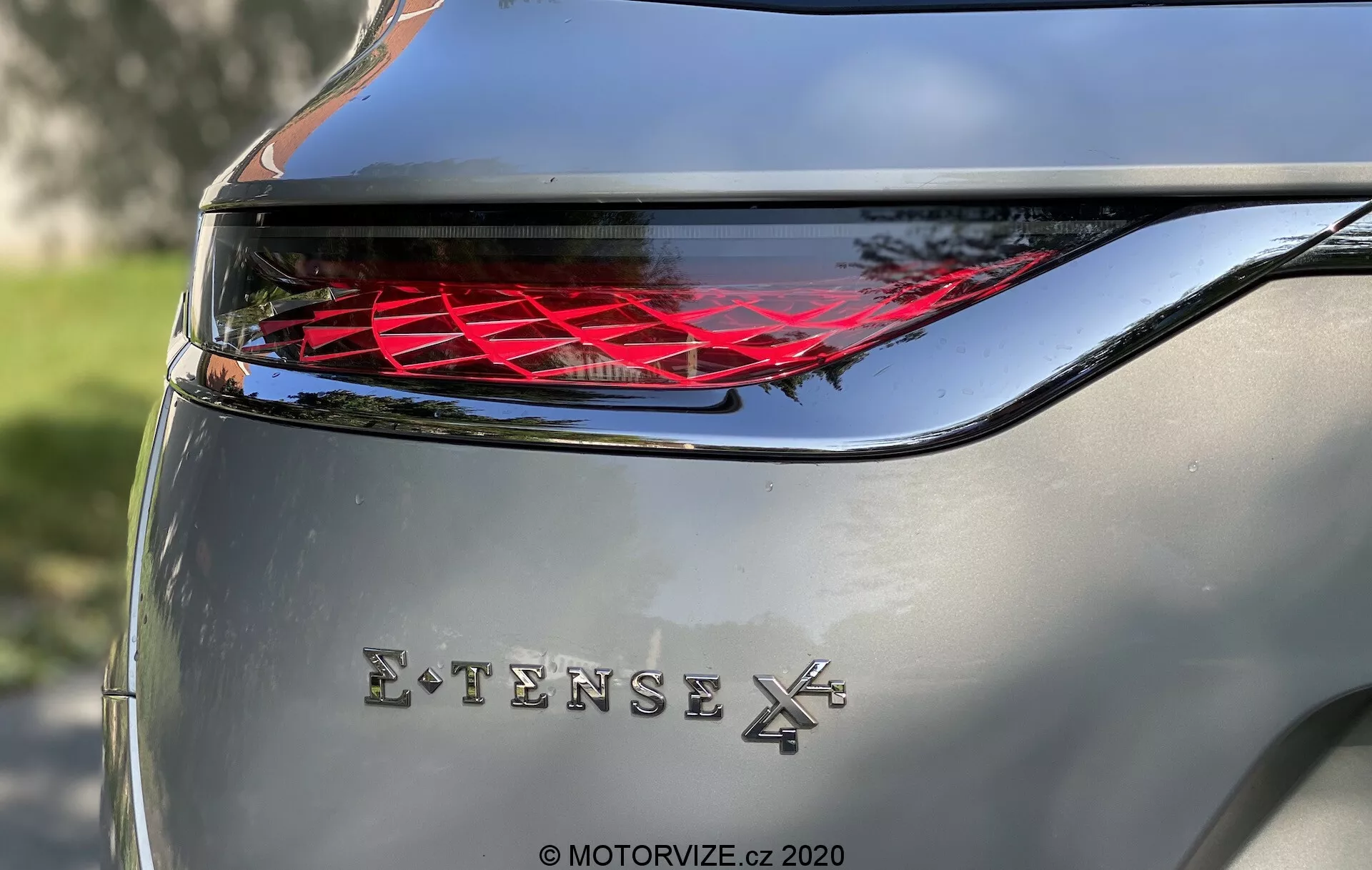 Zbliżenie tylnej części DS Automobiles DS-7 2018 (DS-7 Crossback) pokazujące skomplikowaną tylną lampę LED z poziomą krzywizną i chromowanym oznaczeniem 'EXTENSE 4X', podkreślające zaawansowane technologicznie oświetlenie samochodowe i napęd na cztery koła. Zdjęcie w naturalnym świetle dziennym z srebrnym nadwoziem.