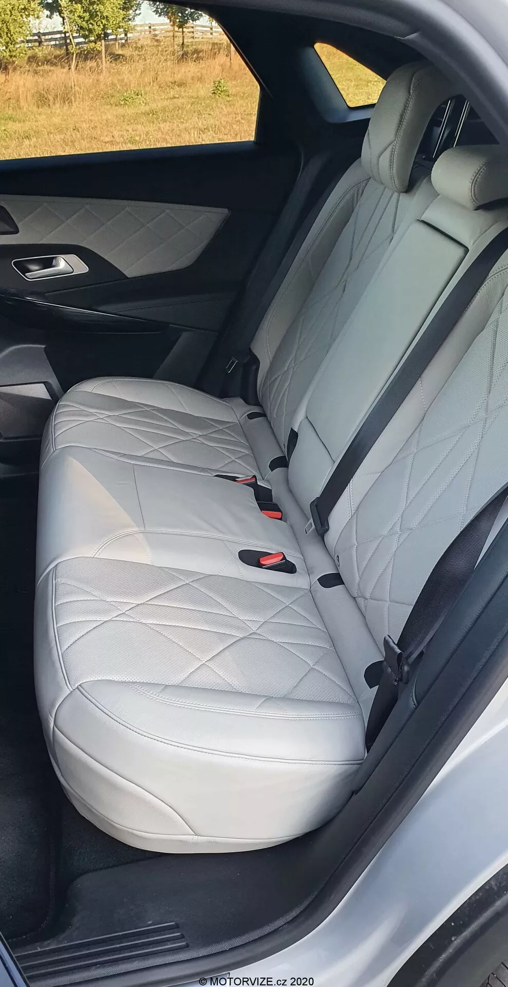 Zbliżenie tylnego siedzenia pasażera DS Automobiles DS-7 2018, pokazujące białą skórę z przeszyciem w kształcie rombu, zagłówek, trzypunktowy pas bezpieczeństwa i system LATCH, podkreślające luksusowy design wnętrza i funkcje bezpieczeństwa samochodu