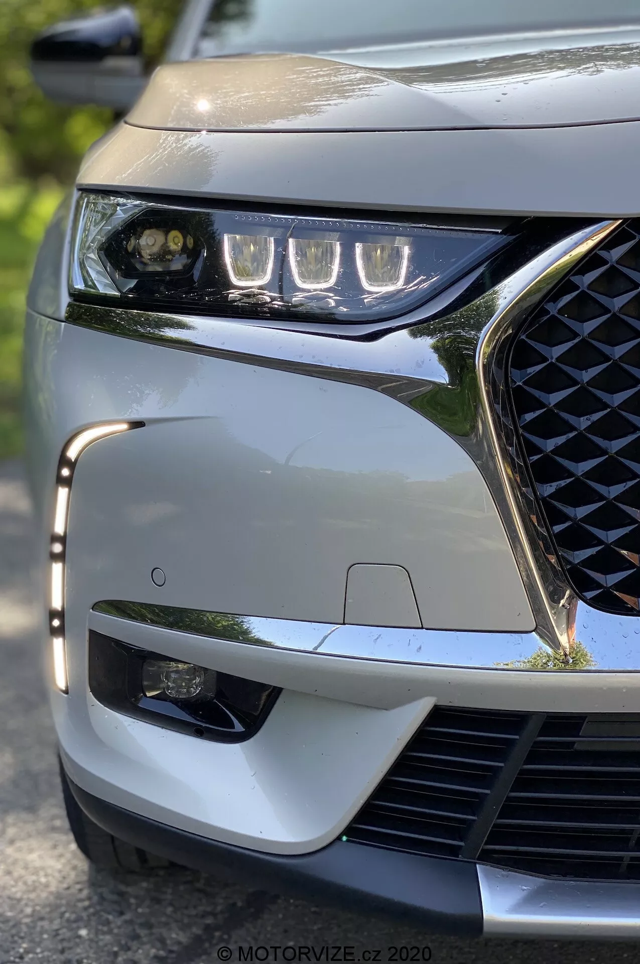 Zbliżenie pod niskim kątem na lewy przedni narożnik modelu DS Automobiles DS 7 Crossback z 2018 roku. Wyróżnione są eleganckie reflektory LED, kratka grilla z geometrycznym wzorem, sportowy przedni zderzak i widoczny czujnik ADAS, podkreślając nowoczesne cechy technologiczne i estetyczne pojazdu.