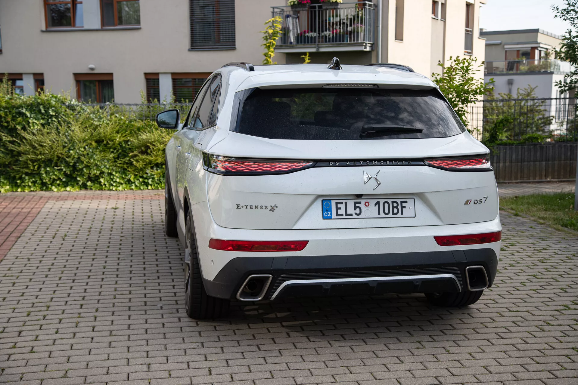 Tylny widok DS Automobiles DS 7 2022 zaparkowanego na bruku z mieszkalnym tłem, pokazujący logo trójzębu, nazwę modelu Levante, emblemat wersji S, światła tylne LED, podwójne chromowane końcówki wydechu, czarny dyfuzor, dużą tylną szybę z wycieraczką, europejską tablicę rejestracyjną, czujniki parkowania, emblemat systemu napędu na wszystkie koła Q4 i antenę płetwy rekina.