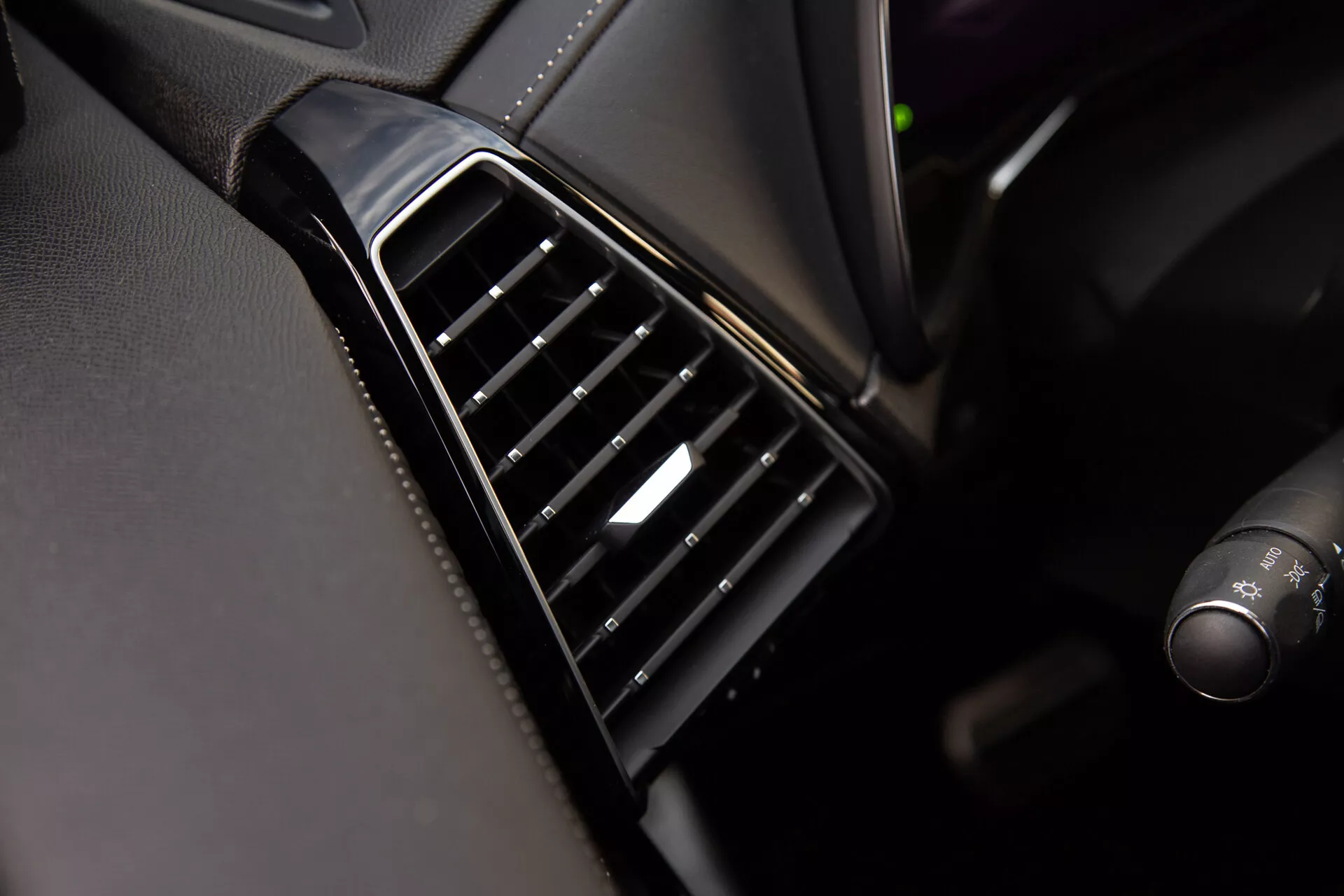Zbliżenie na nawiew powietrza DS Automobiles DS-7 2022 na desce rozdzielczej z czarnymi, regulowanymi listwami ułożonymi pionowo, błyszczącą obwódką i srebrnym akcentem na sterowaniu, prezentujące jakość projektowania wnętrza i materiałów pojazdu