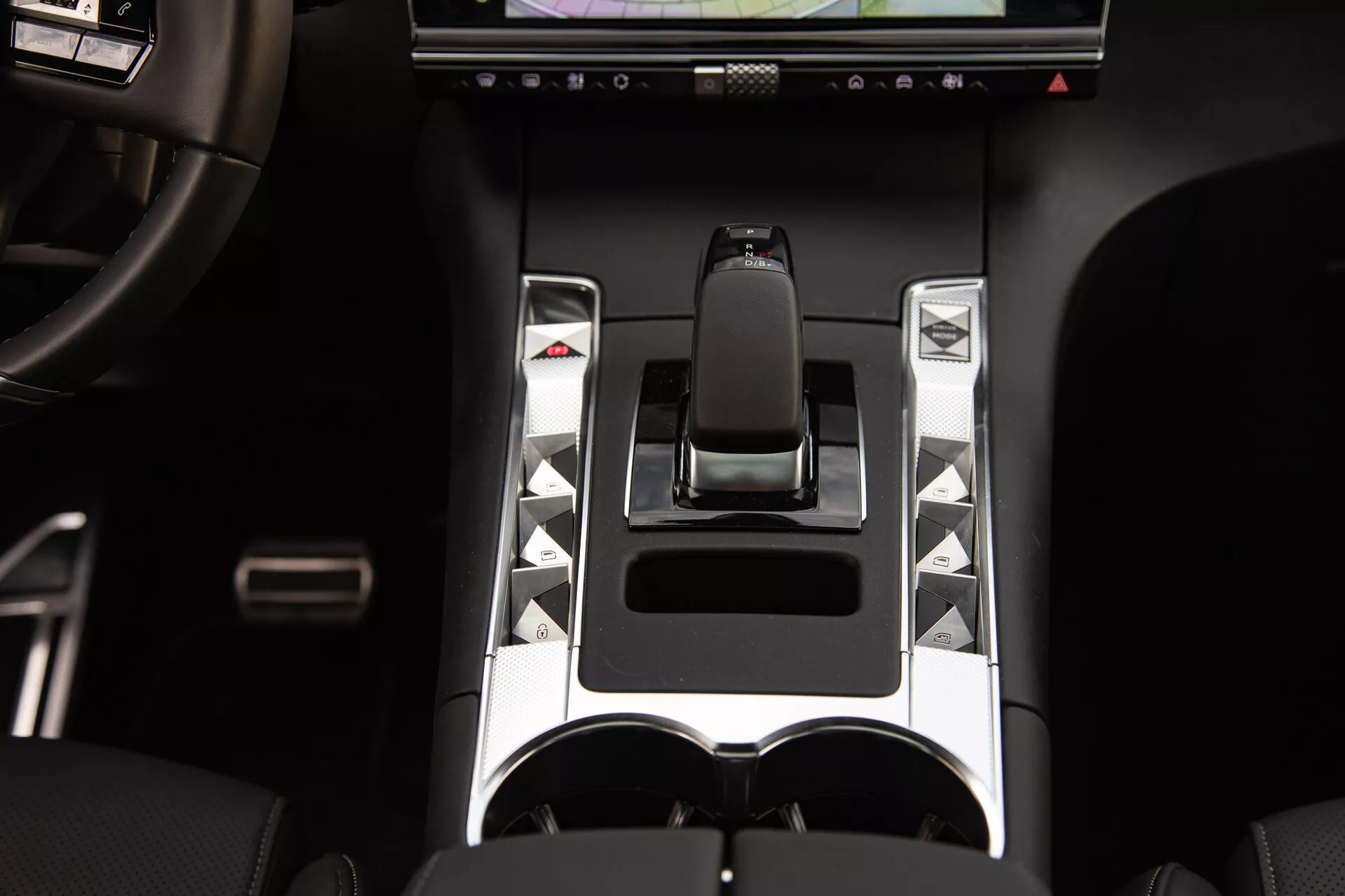 Szczegółowy widok konsoli środkowej DS Automobiles DS-7 2022 z ergonomiczną dźwignią zmiany biegów, metalicznymi akcentami, unikalnymi przyciskami sterującymi, wyświetlaczem dotykowym i podwójnymi uchwytami na napoje, podkreślając zaawansowane elementy kontroli pojazdu i elementy luksusowego designu.