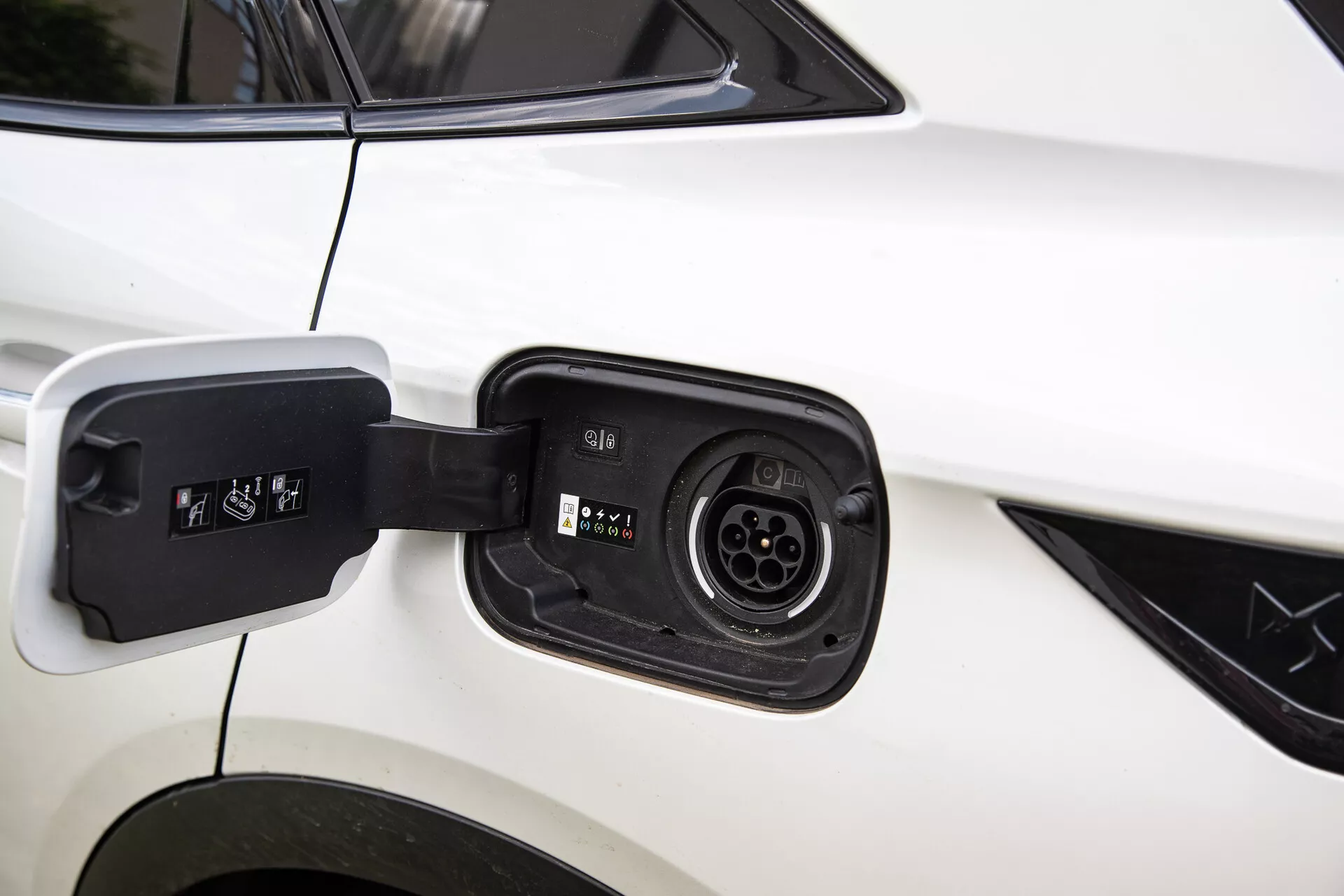 Zbliżenie na port ładowania hybrydowego elektrycznego pojazdu DS Automobiles DS-7 2022, ukazujące kompatybilność z wieloma złączami ładowania na tle białego nadwozia