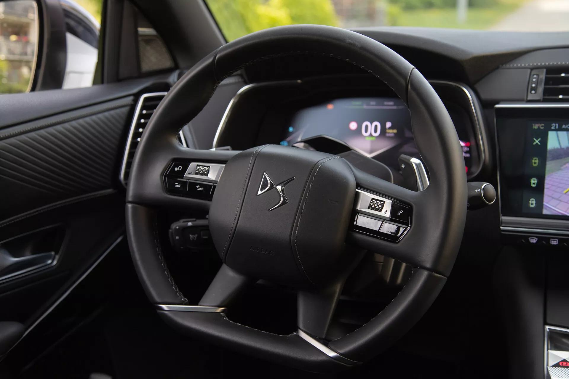 Widok wnętrza DS Automobiles DS-7 2022 pokazujący kierownicę z przyciskami wielofunkcyjnymi i cyfrowy zestaw wskaźników, w tym łopatki zmiany biegów i część systemu infotainment pokazującą nawigację