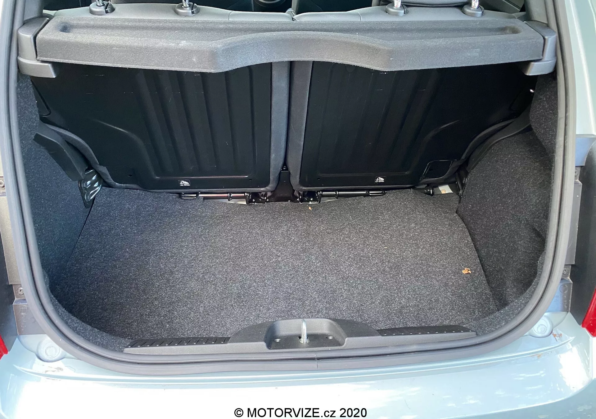 Zbliżenie na przestrzeń bagażową Fiat 500 z 2015 roku z tylnym widokiem z otwartą pokrywą, pokazującą wyściełany dywanem, płaski obszar ładunkowy z plastikowymi bocznymi przegródkami i uchwytem na podłodze bagażnika. Obraz podkreśla przestronność, użyteczność oraz czysty i dobrze oświetlony stan bagażnika.