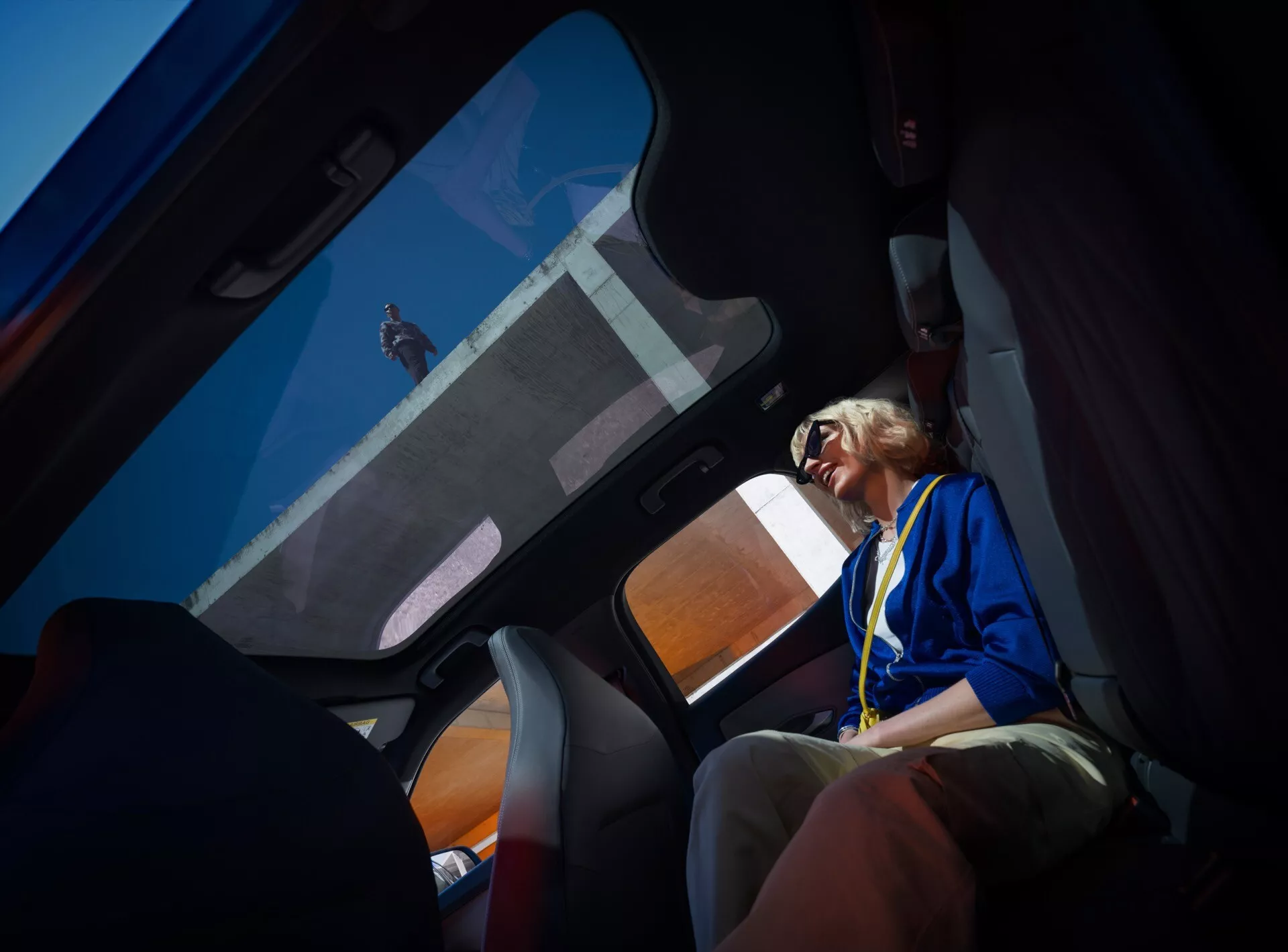 Widok wnętrza Ford Capri 2024 (4. generacja) z perspektywy tylnych pasażerów, ukazujący panoramiczny szyberdach, część tylnego siedzenia, drzwi pasażera przedniego z wykończeniem wysokiej jakości i tapicerkę tekstylną z kolorowymi akcentami.