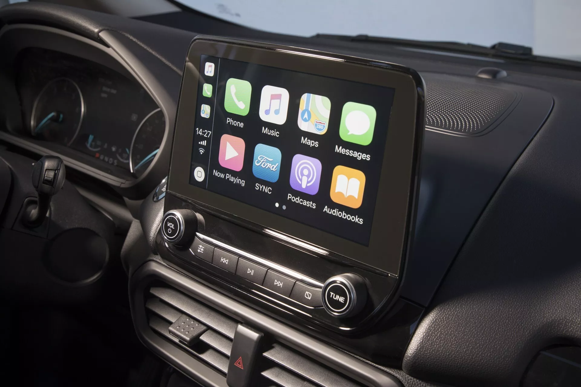 Widok wnętrza Forda EcoSport facelift 2017 skupiający się na systemie infotainment na konsoli środkowej z ekranem dotykowym i integracją ze smartfonem, obok kontroli audio i systemu klimatyzacji dwustrefowej, częściowo widoczna kierownica i zestaw wskaźników.